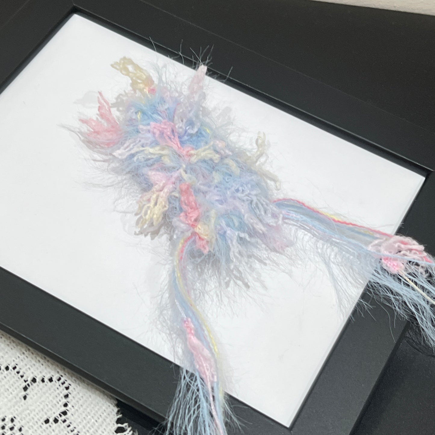 Close-up macro detail of pastel sky pink cream petal layered multi-strand blended fiber mounted on black display frame