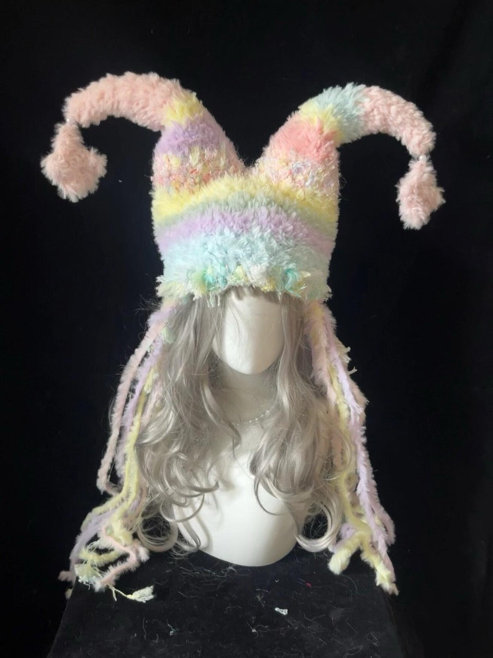 handmade crochet pastel fairycore jester hat in soft rainbow shaggy texture with curly pointed tips and long trailing strands, kawaii whimsical hat