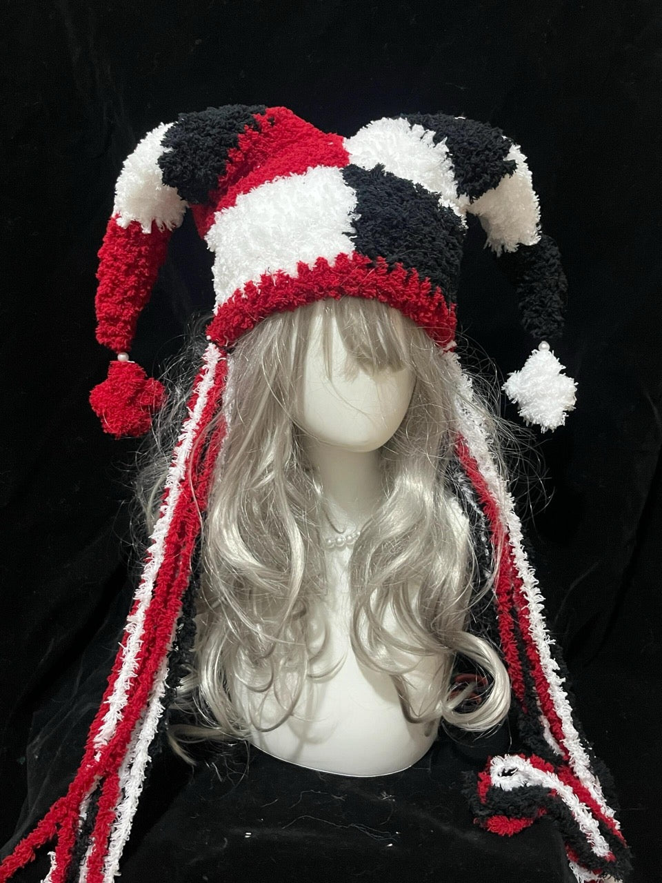 handmade crochet harlequin jester hat in red, white and black diamond pattern with long curved points, pompom tips and long braided ties, circus cosplay hat