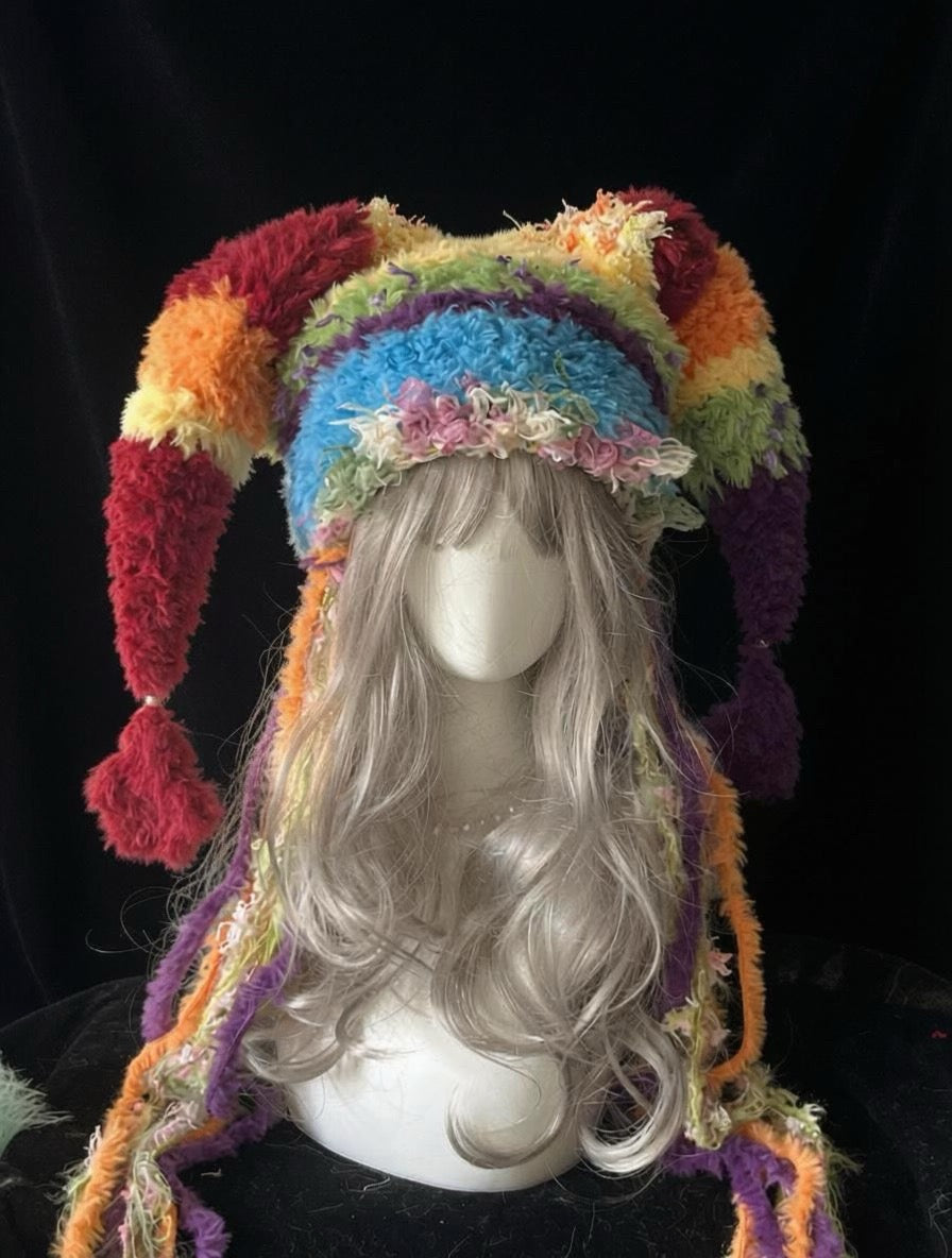 handmade crochet clowncore jester hat in bright rainbow striped shaggy texture with long curved points and pompom tips, festival rave accessory