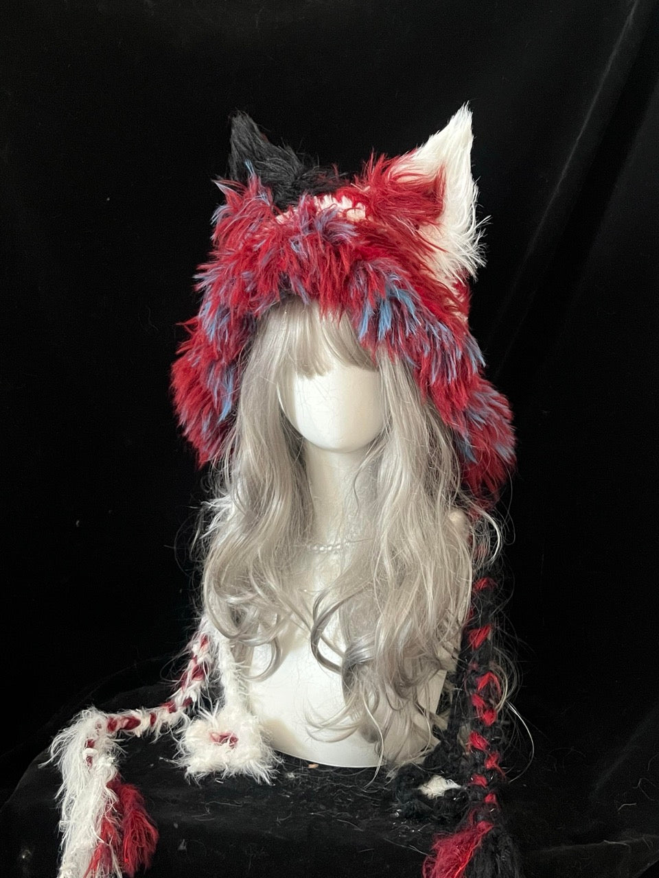 handmade crochet harlequin fox ear hood in bold red, white, blue and black shaggy texture, with long braided ties for circus cosplay and festival looks