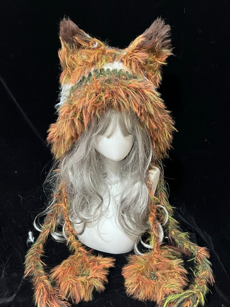 handmade crochet goblincore fox ear hood in orange, green and brown shaggy textured yarn, with long draped sides and braided ties, woodland animal hat for winter styling