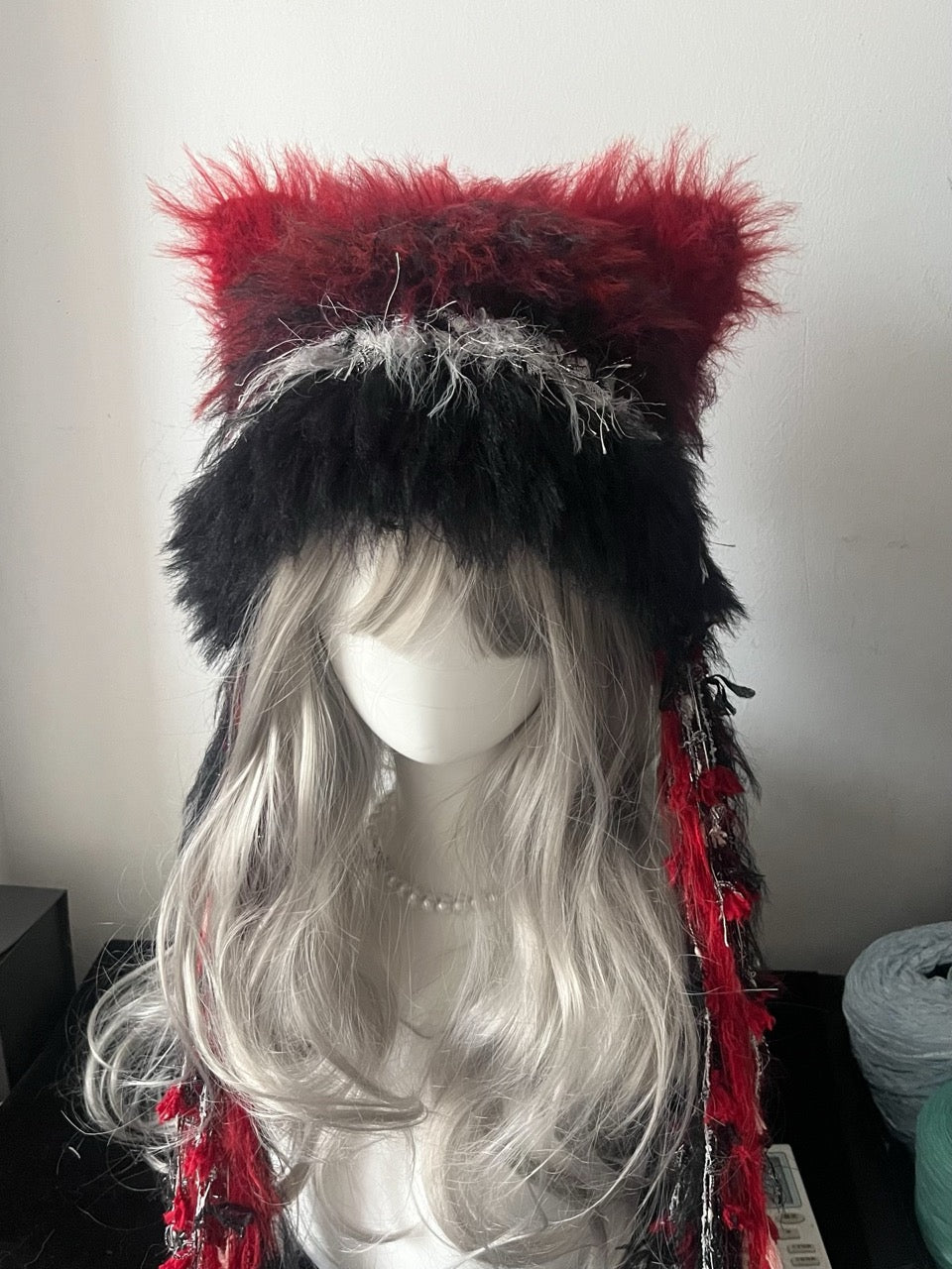 handmade crochet dark fairycore cat ear beanie in bold red and black shaggy faux fur, with tall pointed ears and long trailing tassels, a cozy winter hat for cosplay and festivals