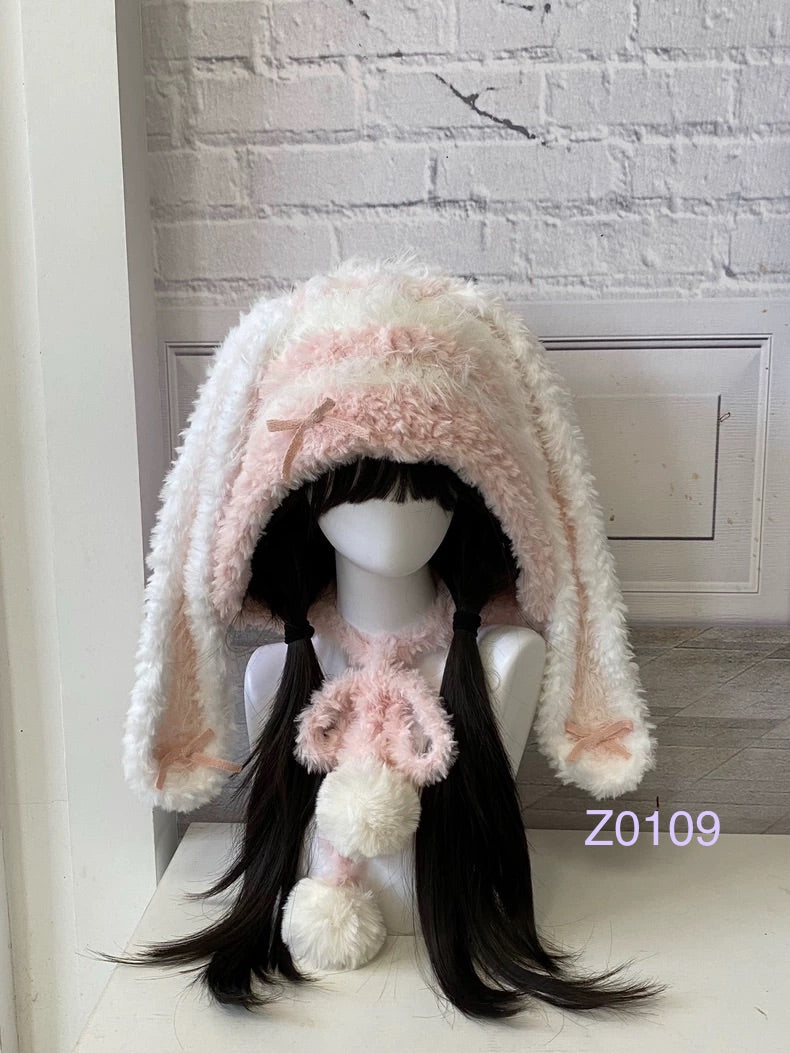 handmade crochet coquette dollette bunny ear hood in soft pink and white fluffy texture with ribbon bows and pompom ties. Fairycore winter headwear for cosplay, photoshoot prop and romantic gift giving