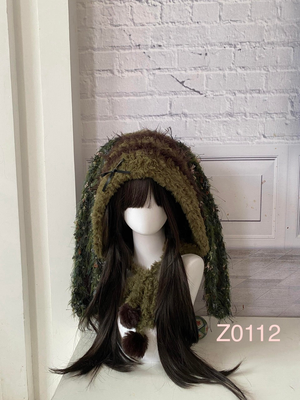 handmade crochet goblincore woodland bunny ear hood in olive green and moss textured yarn with small black ribbon bow and brown pompoms. Cottagecore headwear for cosplay, music festival and photoshoots
