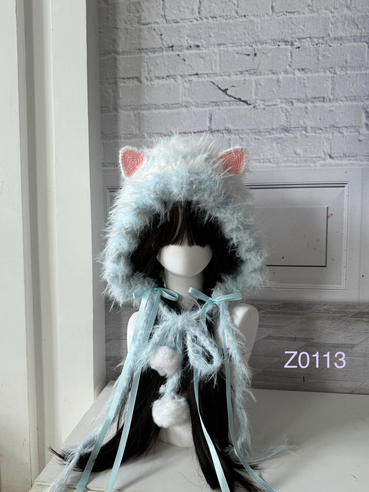handmade crochet kawaii fairycore cat ear hood in soft ice blue fluffy texture with pink inner ears, light blue satin ribbons and white pompom ends. Cozy winter headwear for cosplay, photoshoot prop and gift giving