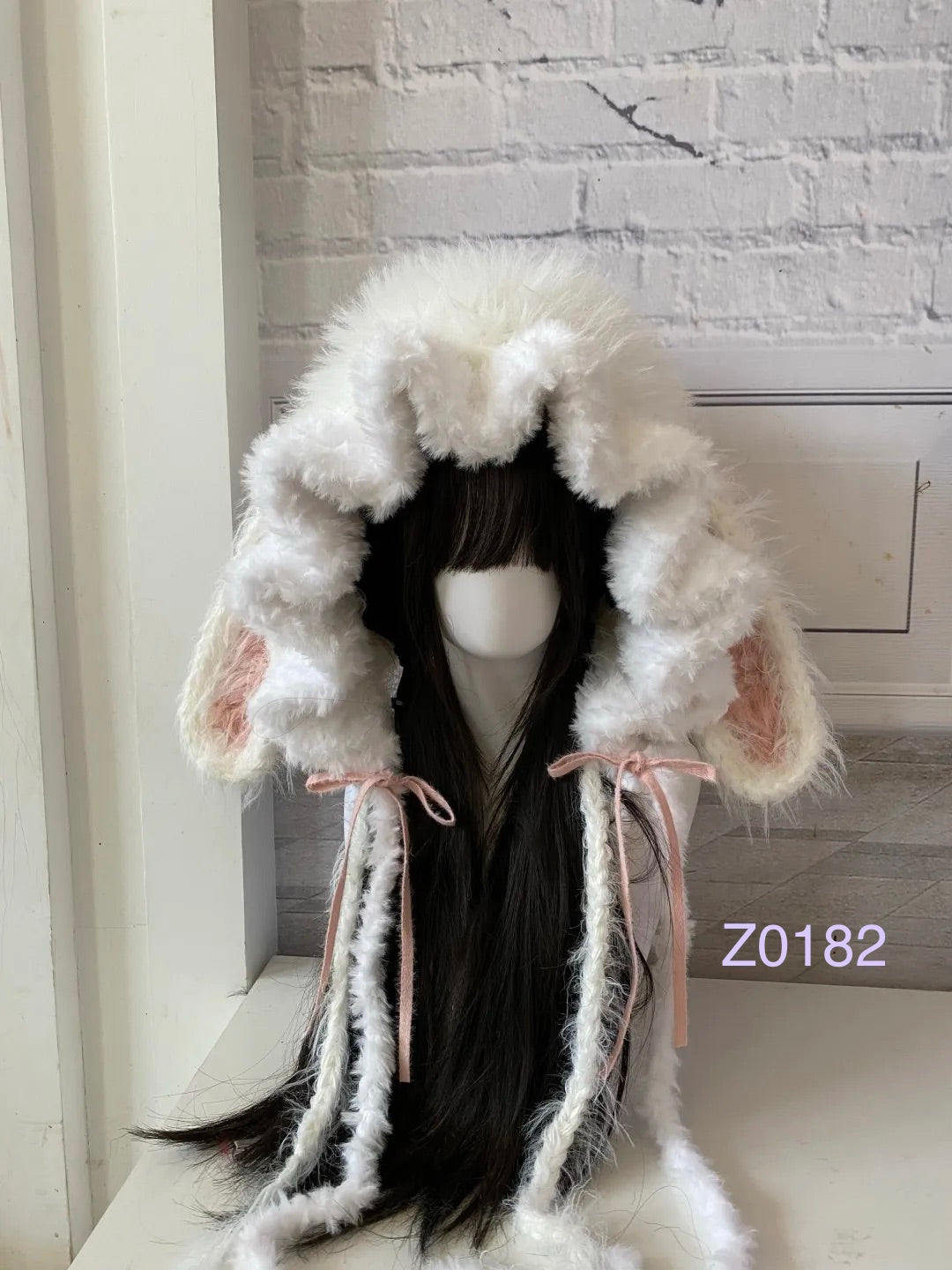 handmade crochet coquette kawaii bunny ear hood in fluffy cream texture with pink inner ears, pink satin ribbons and long trailing pompom ties. Sweet fairycore winter headwear for cosplay, photoshoot prop and gift idea