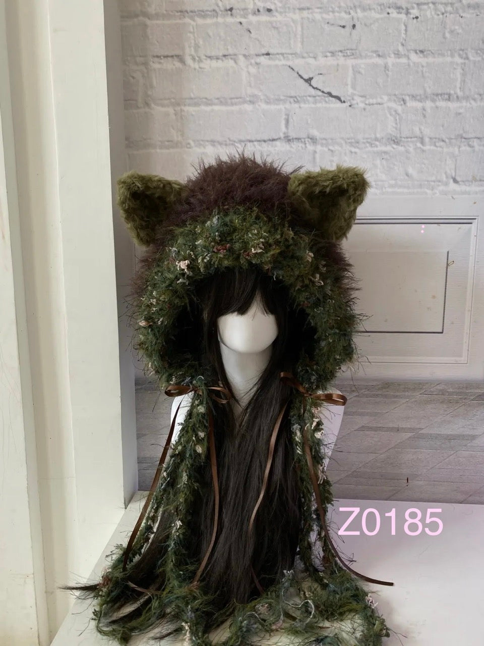 handmade crochet goblincore woodland cat ear hood in dark green and brown floral textured yarn with brown satin ribbon ties and long trailing strands. Cottagecore headwear for cosplay, music festival and photoshoot styling