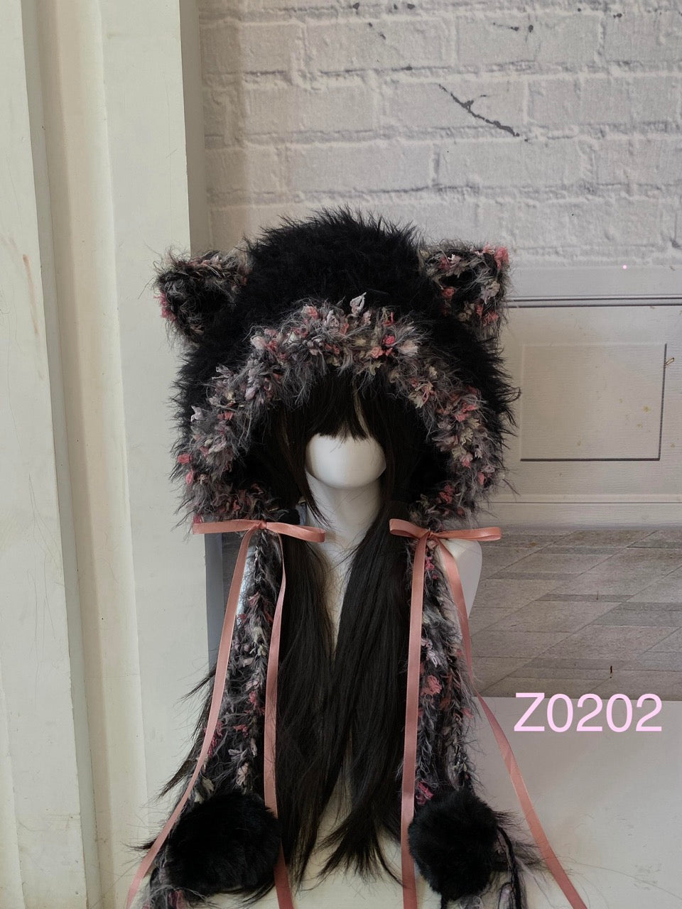 handmade crochet goth coquette cat ear hood in black and pink floral textured yarn, pink satin ribbon bows and black pompom ends. Dark fairy headwear for cosplay, rave party and photoshoot styling