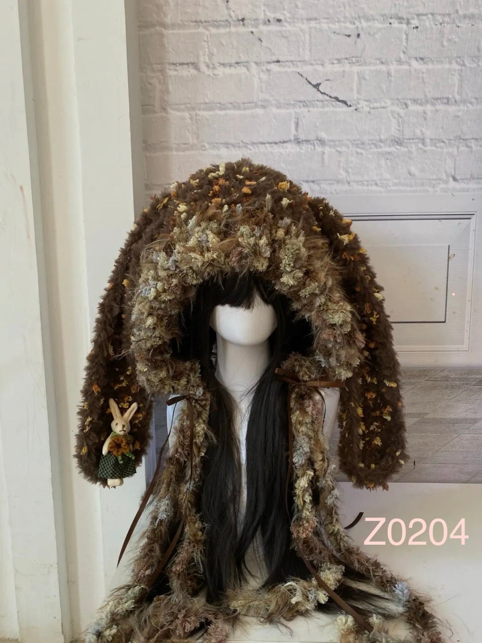handmade crochet storybook woodland bunny ear hood in brown floral textured yarn, accented with a small rabbit doll charm. Whimsical animal hood for cottagecore cosplay and gift idea