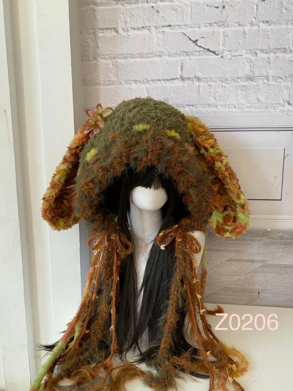 handmade crochet cottagecore goblincore bunny ear hood in forest green and brown textured yarn with small flower details and long trailing ribbons. Woodland fairy headwear for cosplay, music festival and photoshoot styling