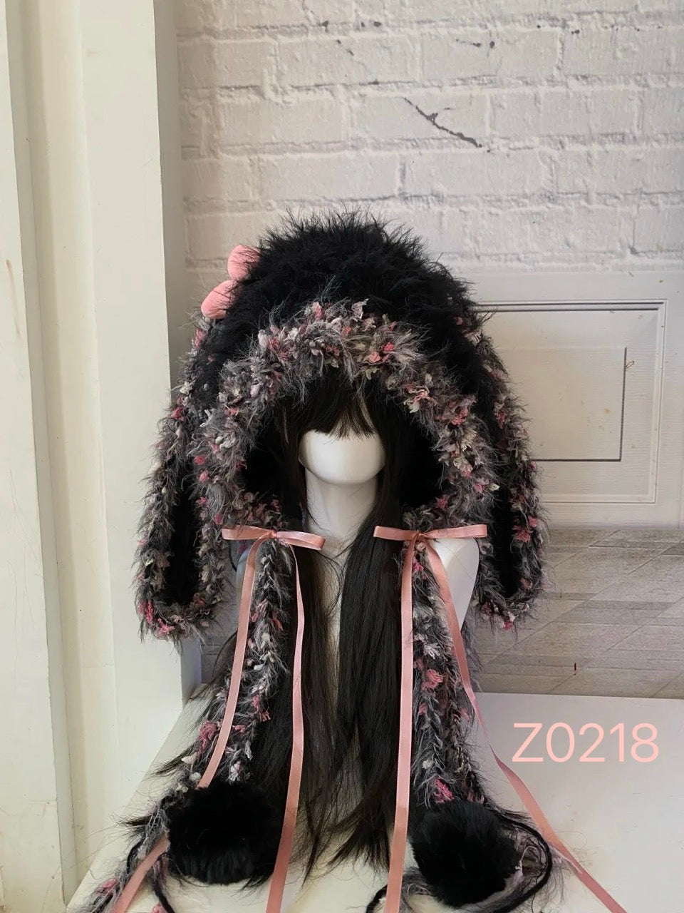 handmade crochet dark fairy goth coquette bunny ear hood in black and pink floral speckled textured yarn, pink satin ribbons and large black fur pom-poms. Whimsical cosplay headwear for rave party and photoshoot styling
