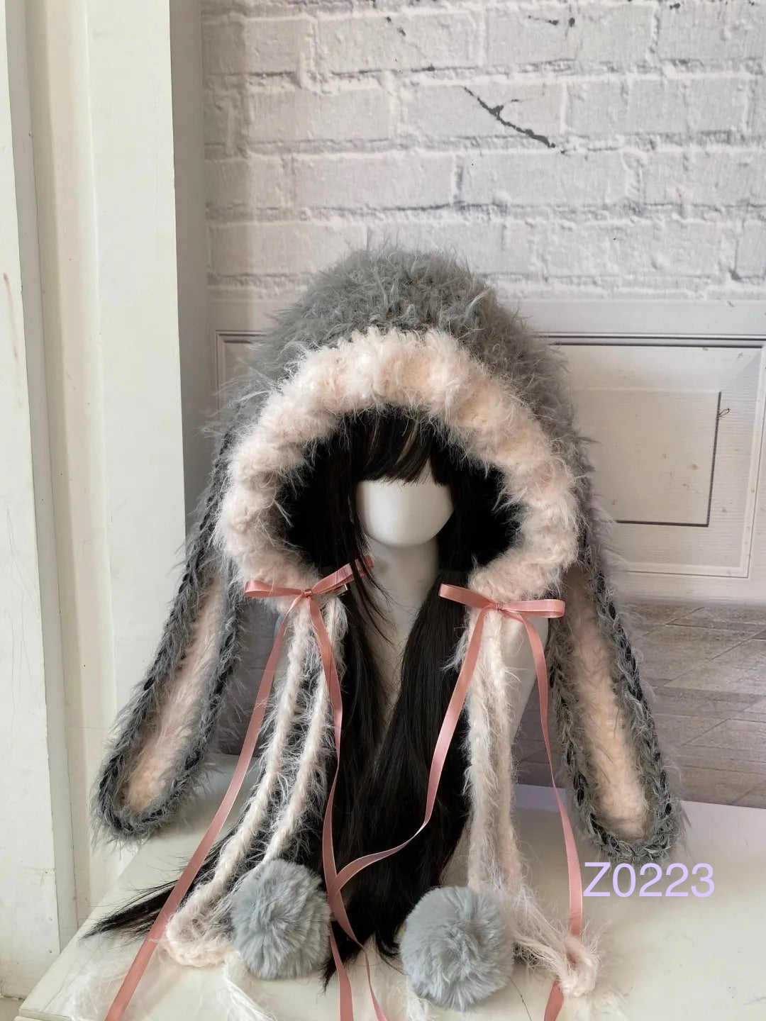 handmade crochet coquette kawaii bunny ear hood with fluffy gray outer texture and pale pink inner trim, pink satin ribbon bows and fur pompoms. Cozy winter headwear for cosplay, photoshoot prop and gift idea