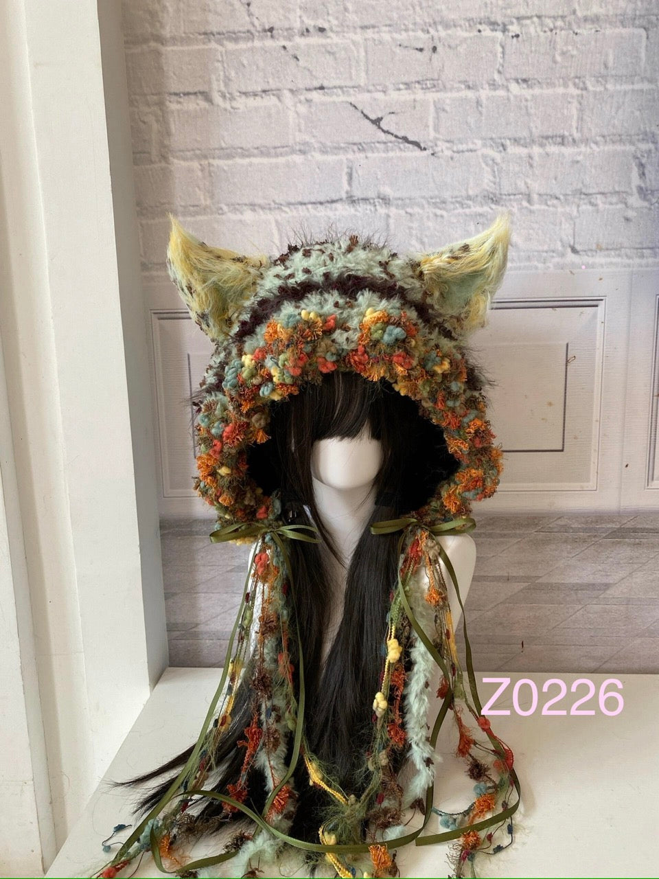 handmade crochet fairycore cottagecore fox ear hood in mint green and orange floral textured yarn with pointed ears, olive satin ribbons and long trailing strands. Woodland headwear for cosplay, music festival and photoshoot styling