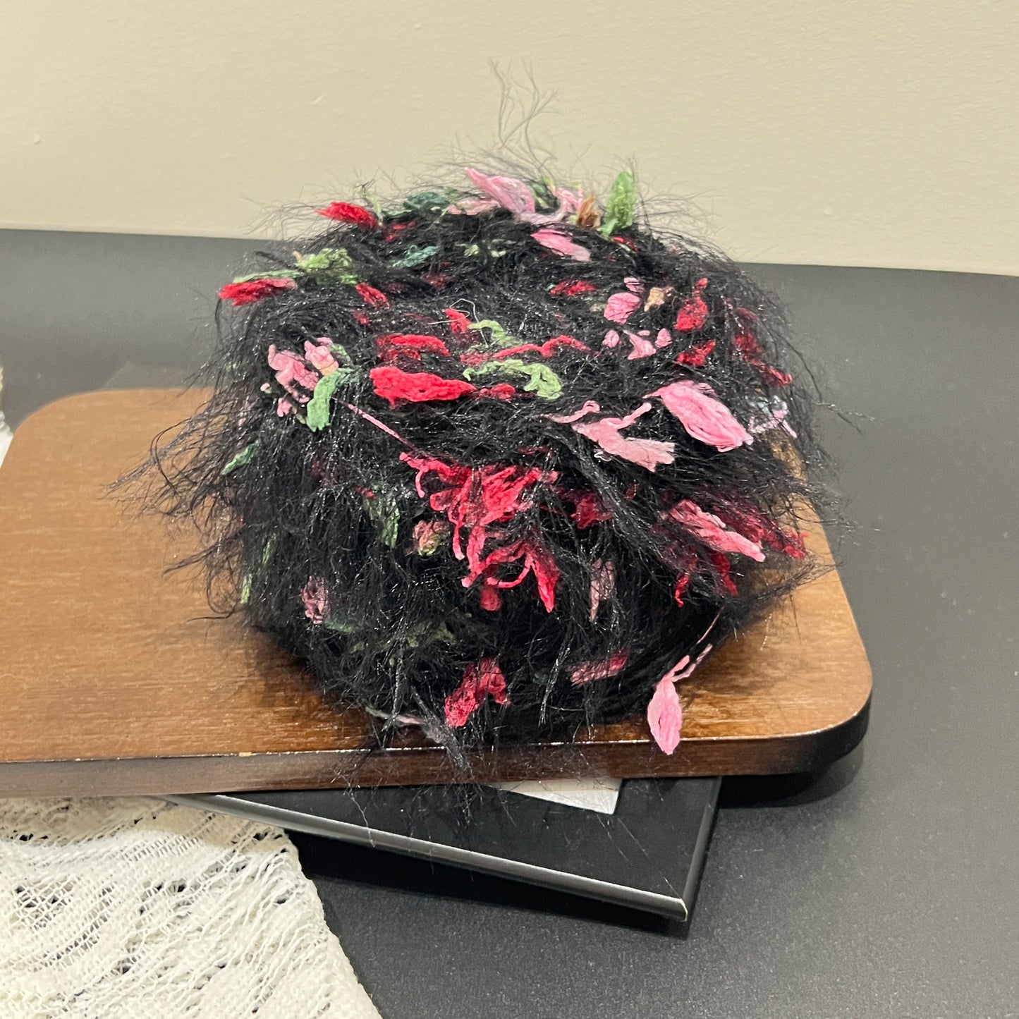 Close-up macro shot black multi-floral fiber swatch mounted inside thin black photo frame, long fuzzy feather yarn and pink red green petal ribbon decorative details