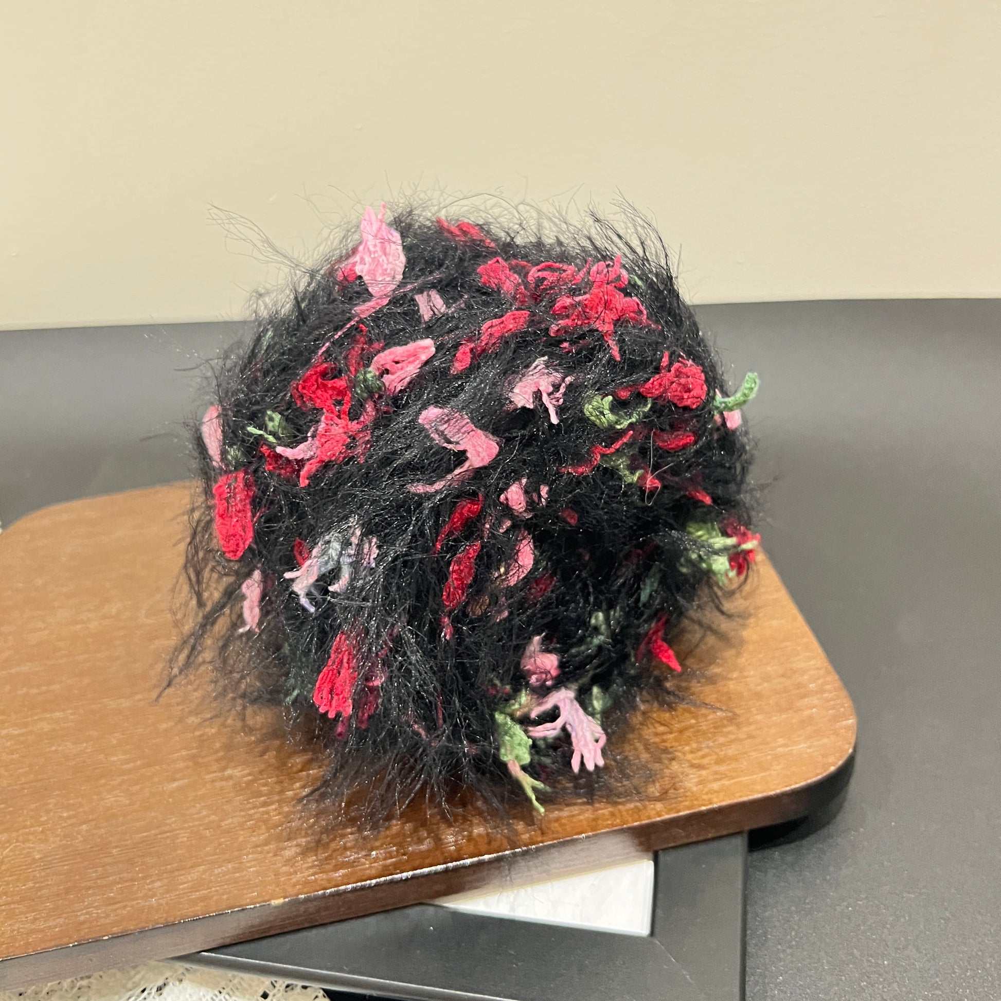 Rotated side overhead shot black rose art yarn cake, distinct layered airy feather and multi-tone floral petal fiber texture fully displayed