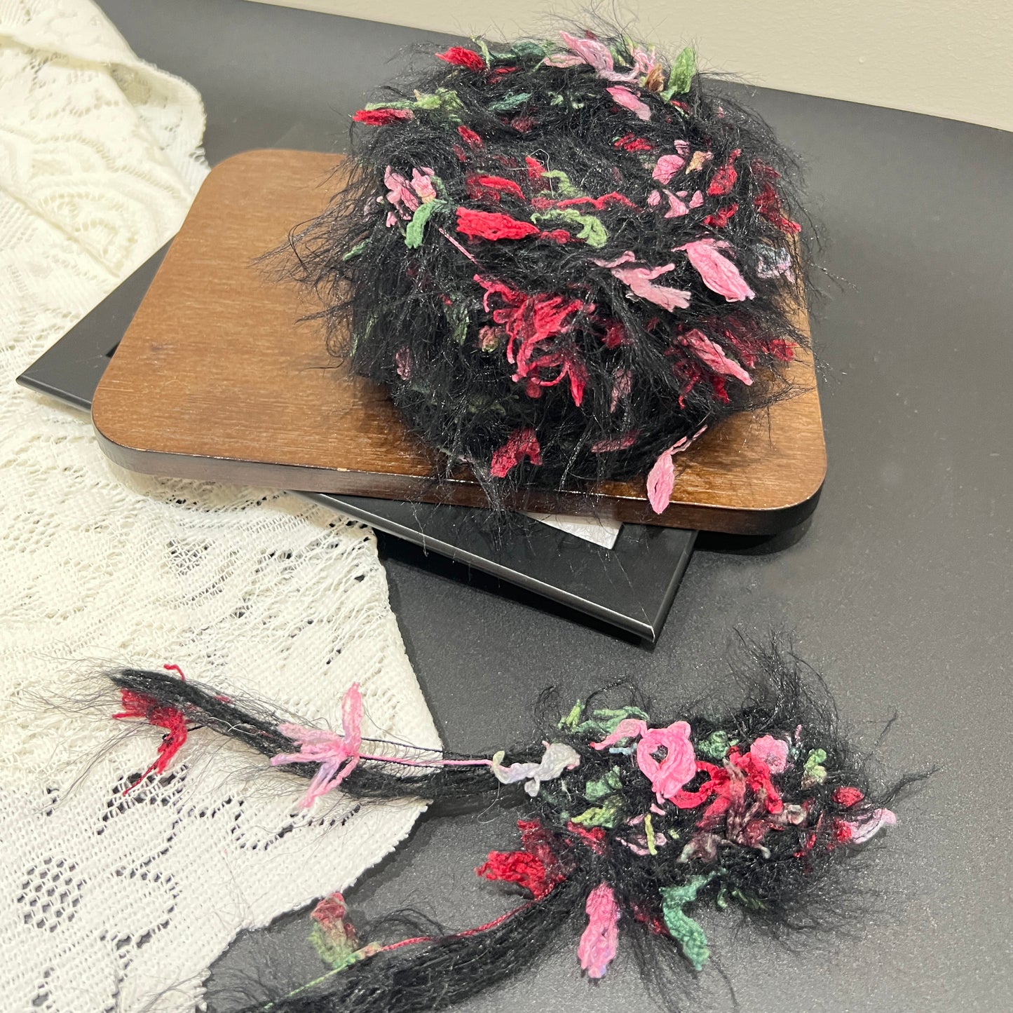 Top-down overhead center view black base yarn cake, evenly distributed pink, red, green decorative petal fiber fragments, fluffy long feather strands fully covering surface