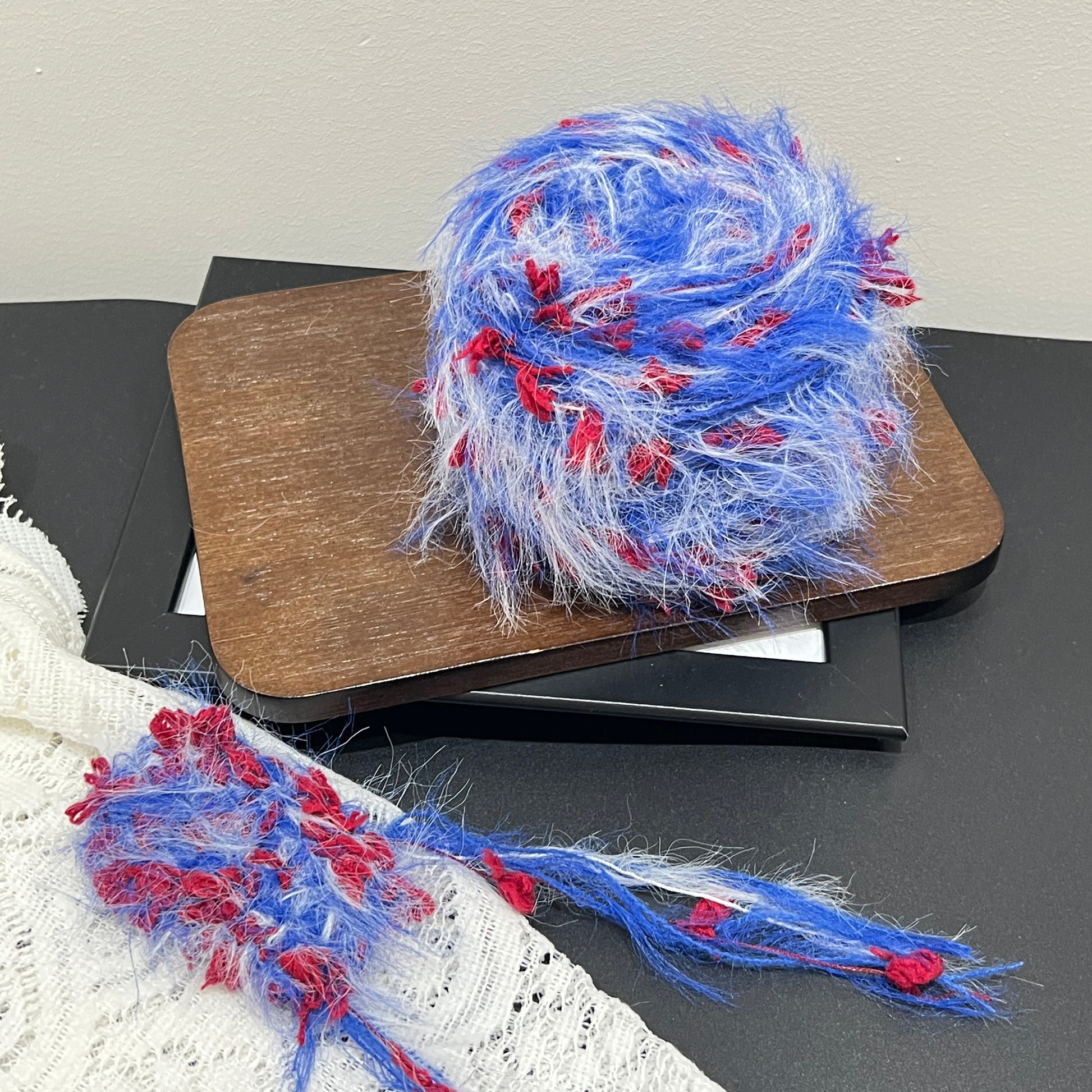 Full layout display set: tri-color yarn ball + detached fiber swatch, perforated white lace fabric laid flat on dark matte countertop surface
