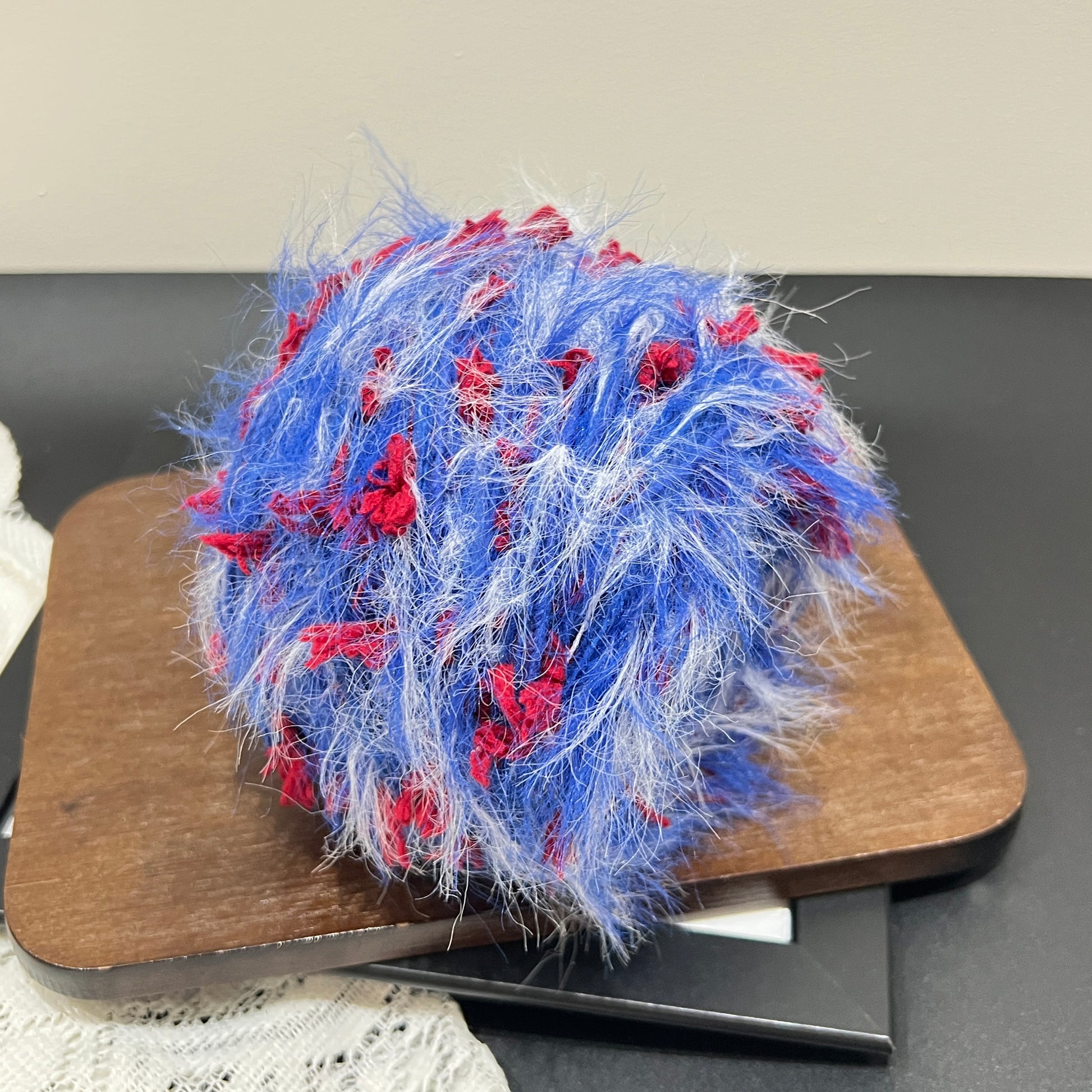 Rotated side overhead shot tri-color art yarn cake, distinct layered airy feather and red petal fiber texture fully displayed