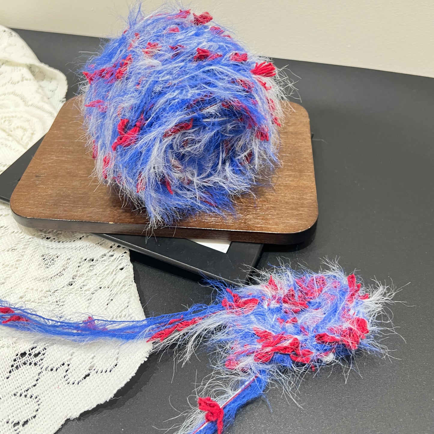 Top-down overhead center view blue red white floral yarn cake, evenly distributed red petal decorative fiber fragments, fluffy long feather strands all over surface