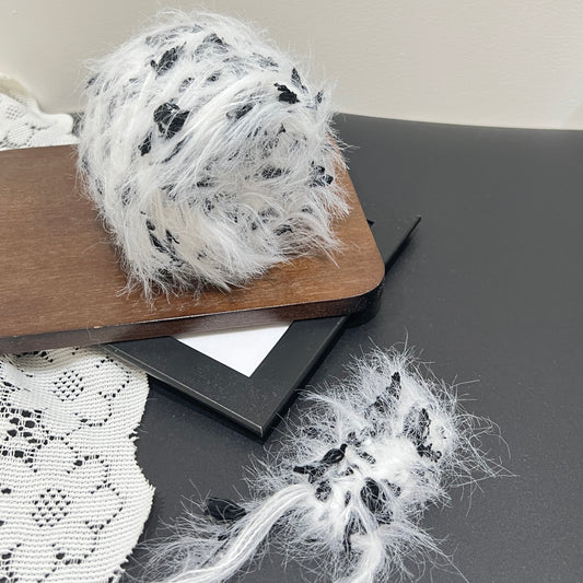 Monochrome black white floral multi-strand hand-blended cake yarn placed on wooden board with white lace fabric backdrop