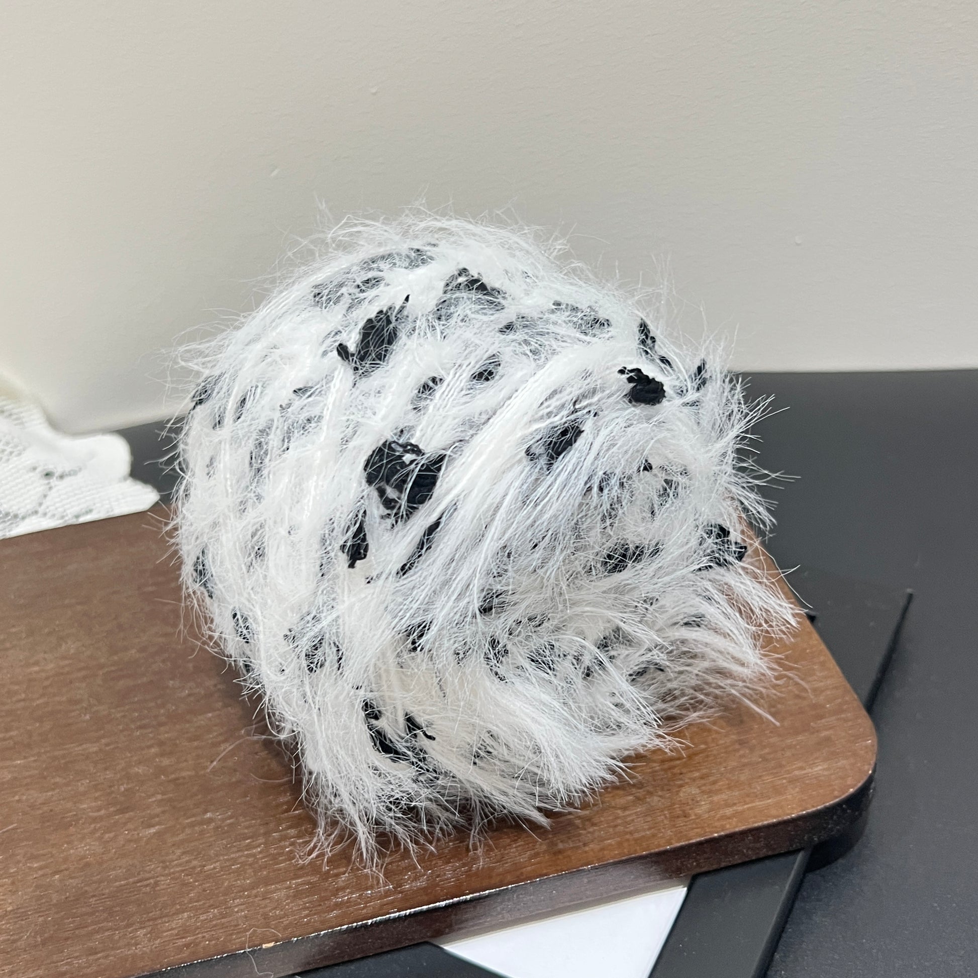 Side angle shot monochrome floral artisan blend yarn cake with scattered black petal fiber accents