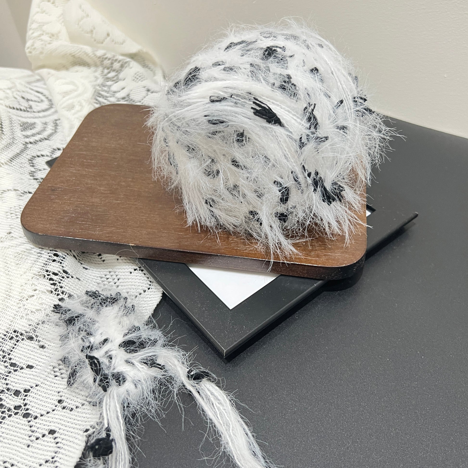 Layout shot monochrome floral yarn cake and matching fiber swatch beside hollow lace fabric on dark countertop