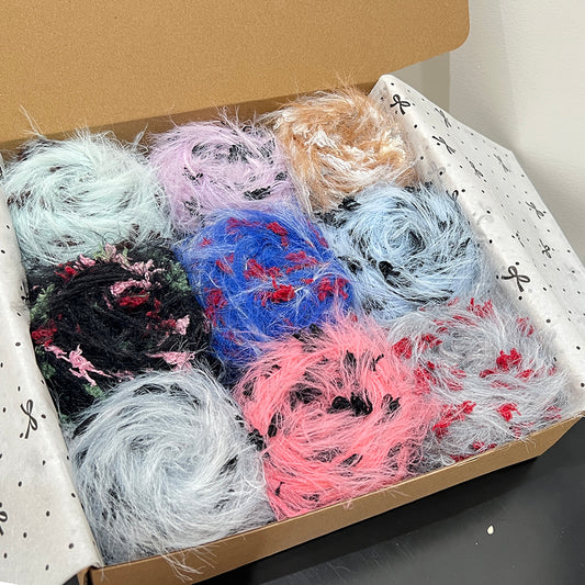 Open gift box with 9 muted contrast floral yarn cakes, black rose, pale gray, bright blue, caramel, blush pink dark accent art yarn assortment inside gift box