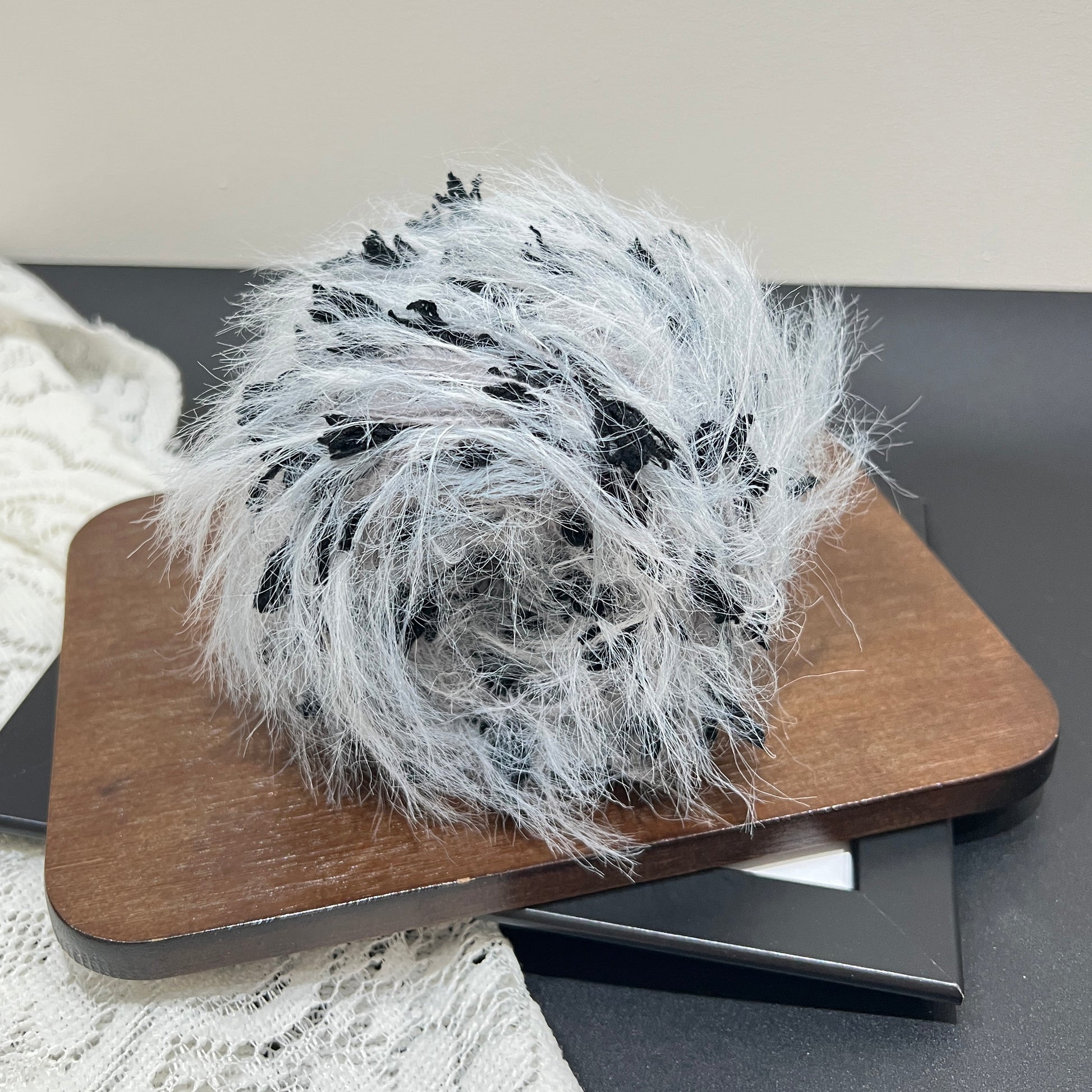 Wide layout shot yarn cake + long tassel fiber swatch, hollow white lace fabric laid on dark tabletop
