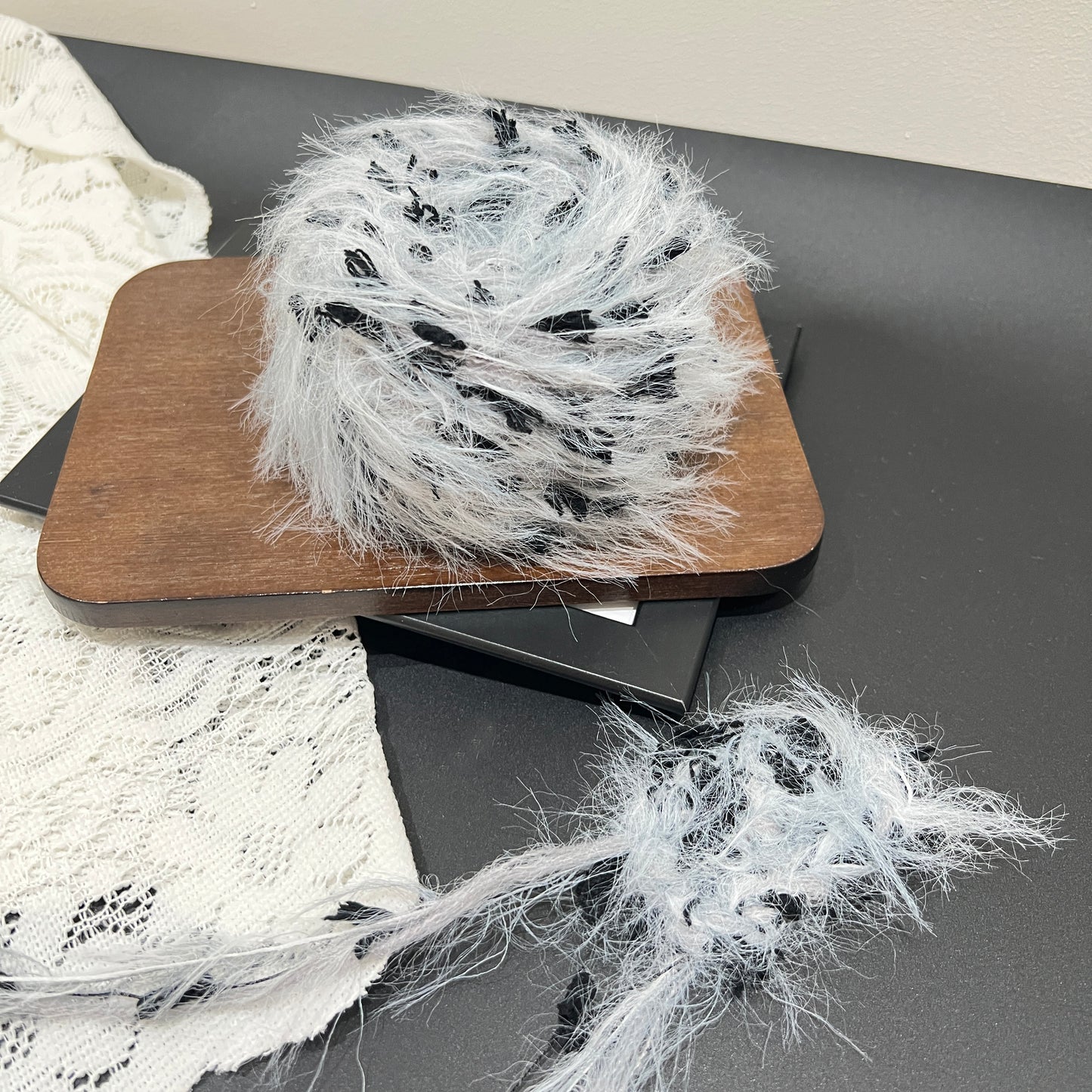 Full layout display set: gray black yarn ball + detached fiber swatch, perforated white lace fabric laid flat on dark matte countertop surface