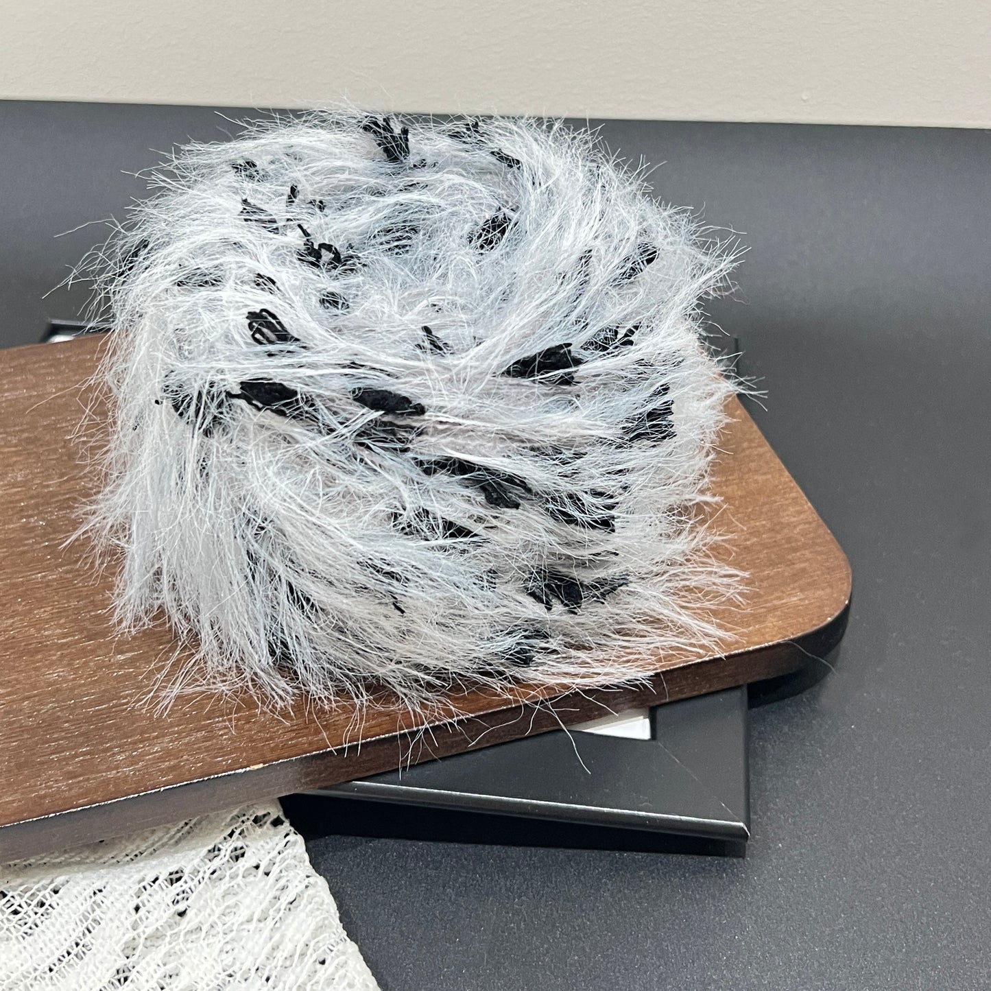 Rotated side overhead shot gray black art yarn cake, multi-tone contrast feather and petal fiber texture fully displayed