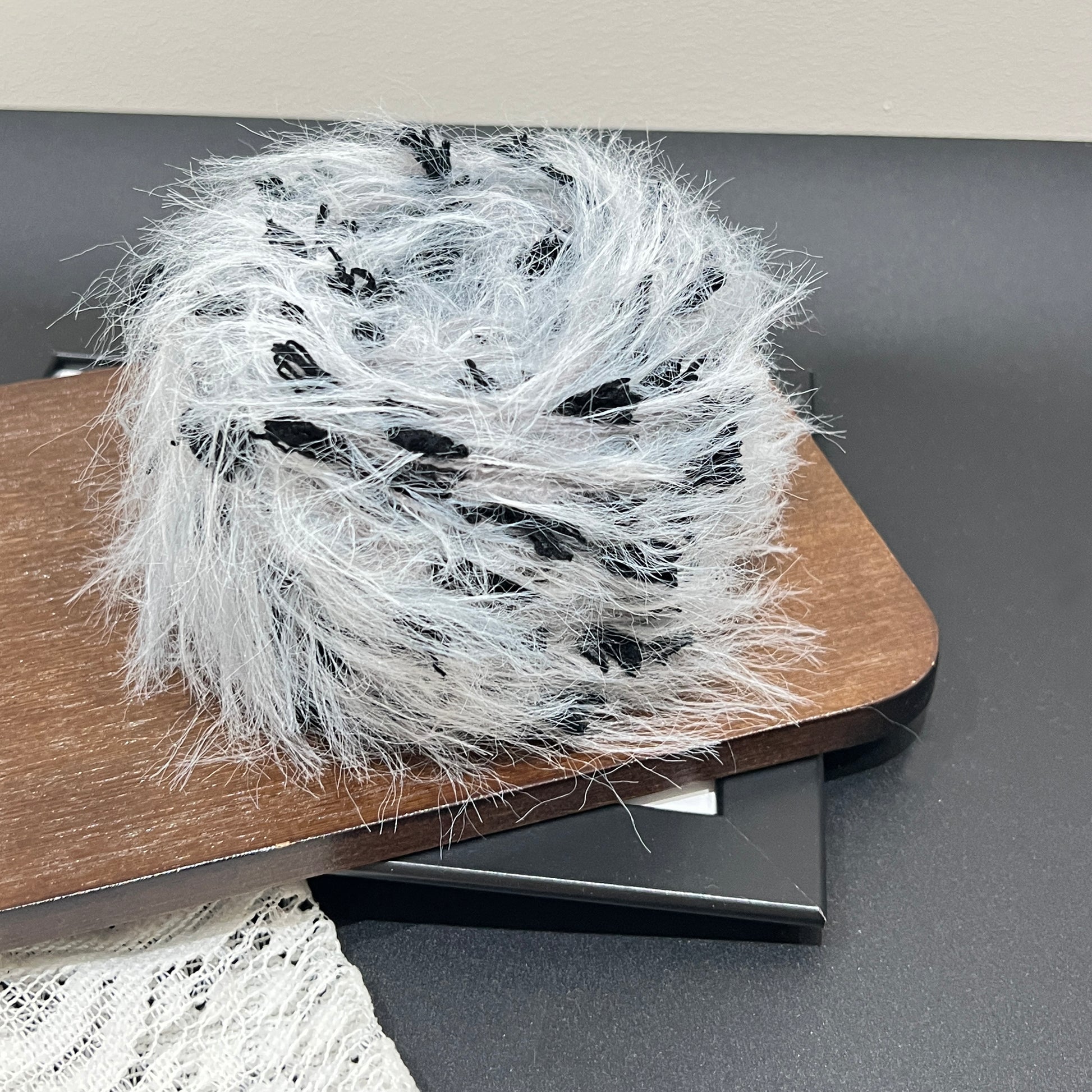Rotated side overhead shot gray black art yarn cake, multi-tone contrast feather and petal fiber texture fully displayed