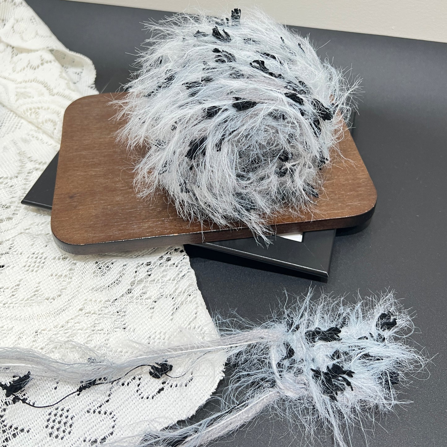 Top-down overhead center view gray black floral yarn cake, evenly distributed solid black petal decorative fiber fragments, fluffy long feather strands fully covering surface