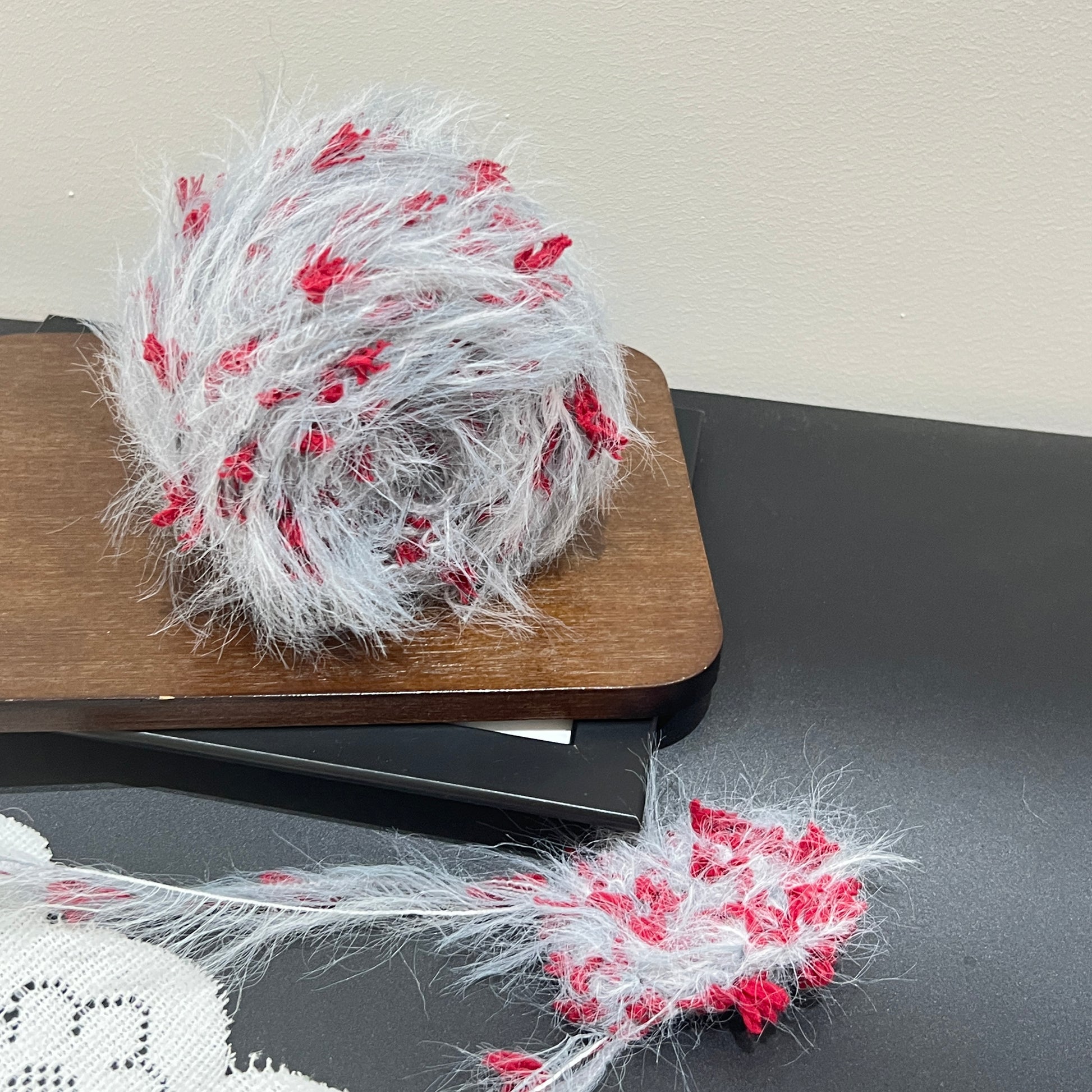 Full layout display: pale gray yarn cake + detached fiber swatch, hollow white perforated lace fabric laid on dark matte countertop surface