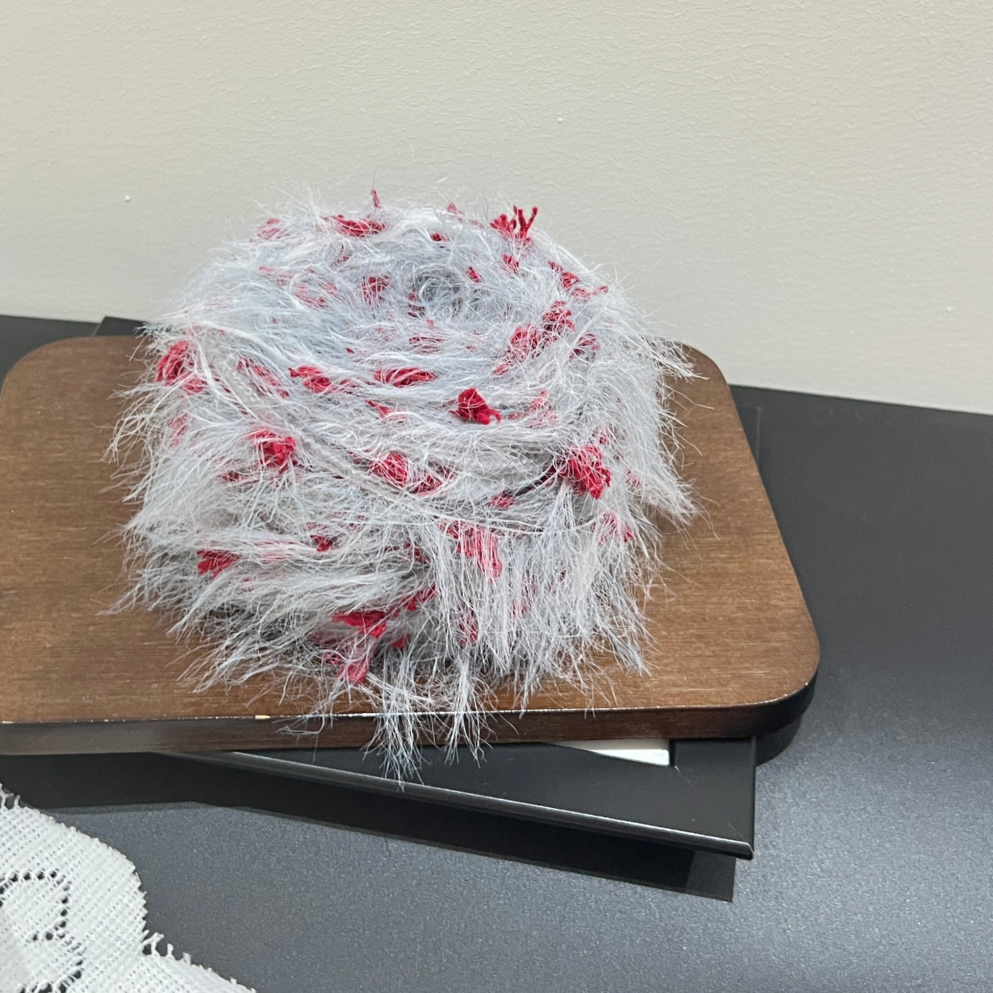 Top-down overhead center view pale gray base yarn cake showcasing evenly distributed scarlet red decorative petal fiber fragments and long fuzzy feather strands