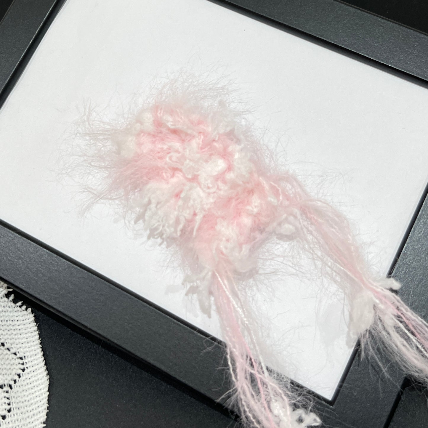 Close-up macro detail of pastel blush white petal layered multi-strand blended fiber on black display frame