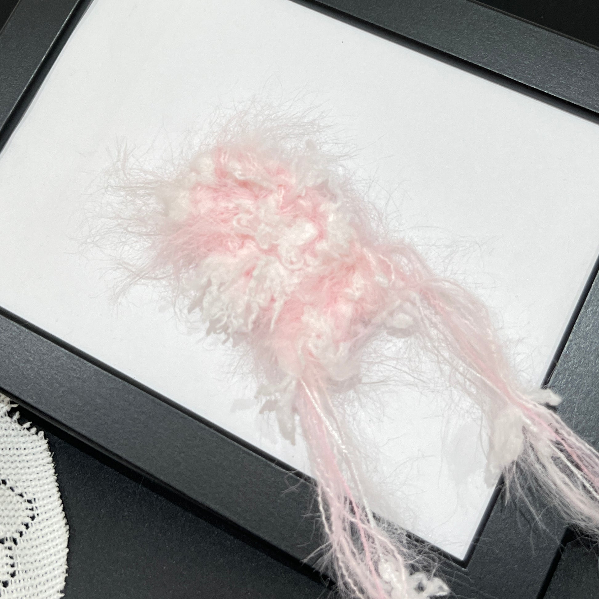 Close-up macro detail of pastel blush white petal layered multi-strand blended fiber on black display frame