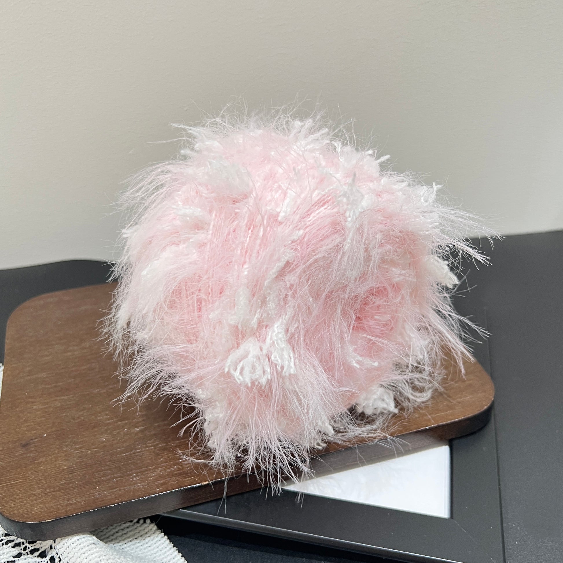 Front perspective pastel blush white multi-strand blended yarn cake with scattered white petal fiber accents