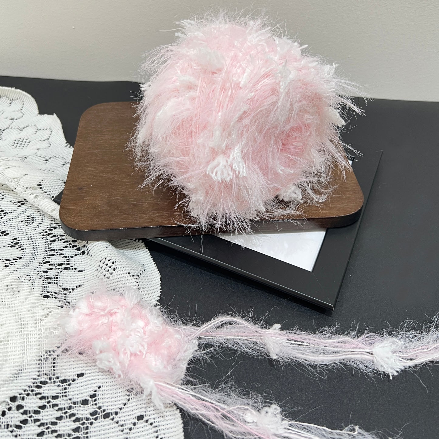 Pastel blush white floral multi-strand hand-blended cake yarn placed on wooden board with plain neutral backdrop