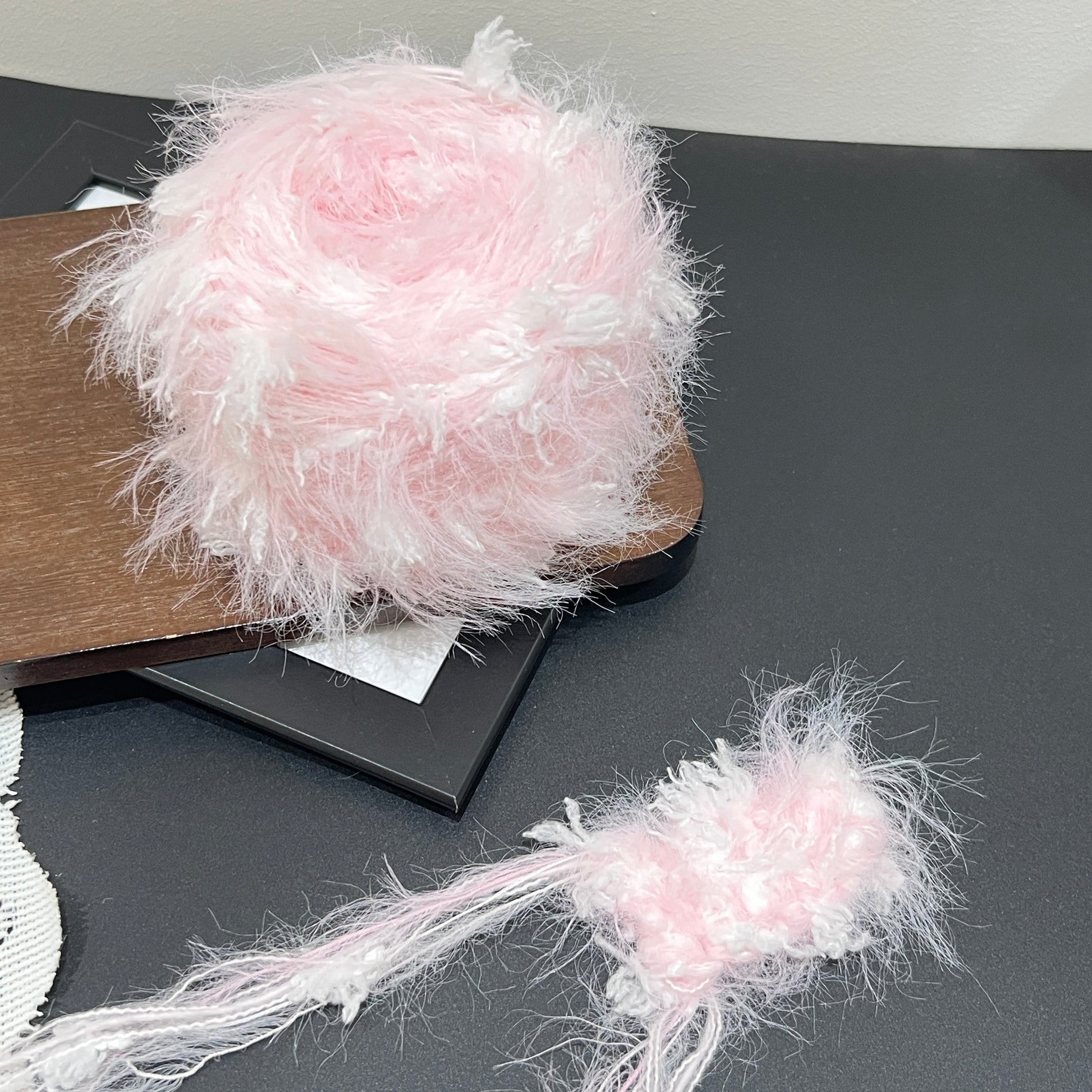 Layout shot of pastel blush floral yarn cake and fiber swatch beside white lace fabric on dark countertop