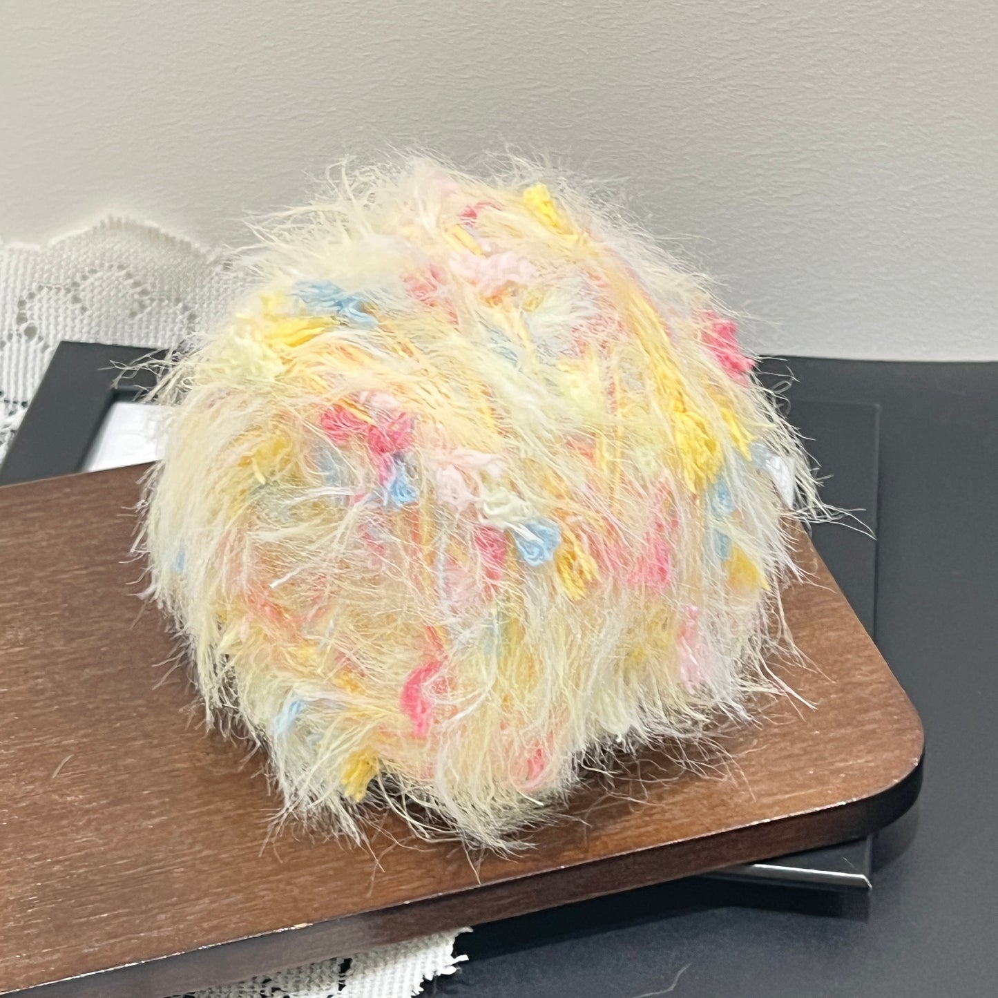 Top-down overhead center view multi-pastel floral yarn cake, evenly distributed pink, blue and yellow decorative petal fiber fragments, fluffy long feather strands