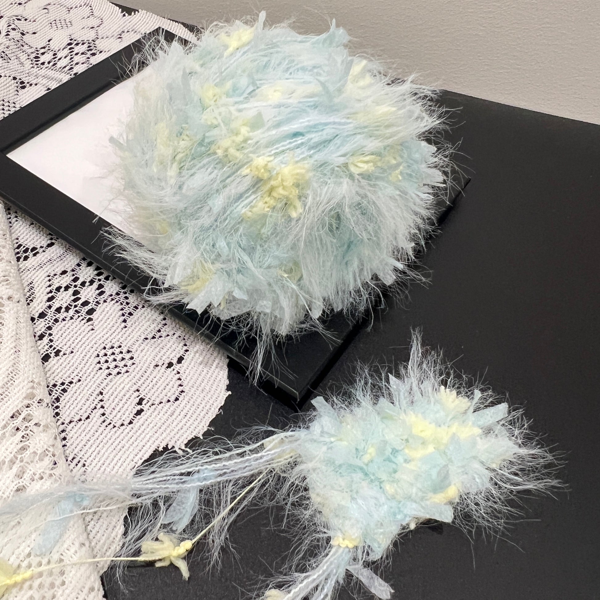 Front overhead round view pastel cyan yellow layered floral hand-blended cake yarn on black display frame