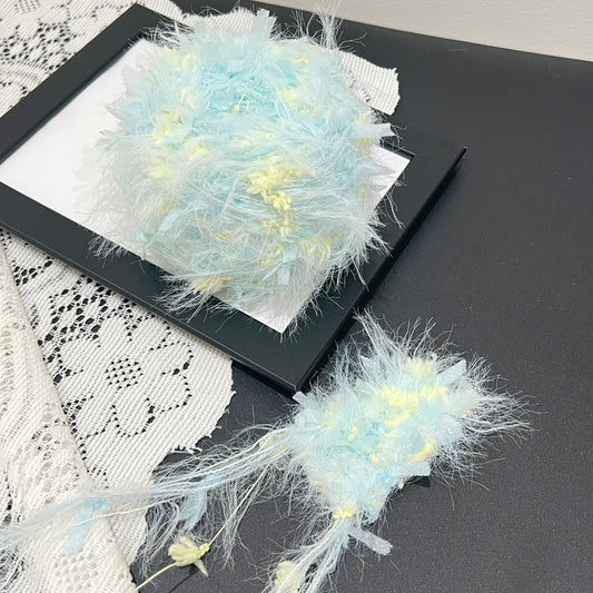 Pastel cyan yellow floral multi-strand hand-blended cake yarn placed on black frame with white lace backdrop