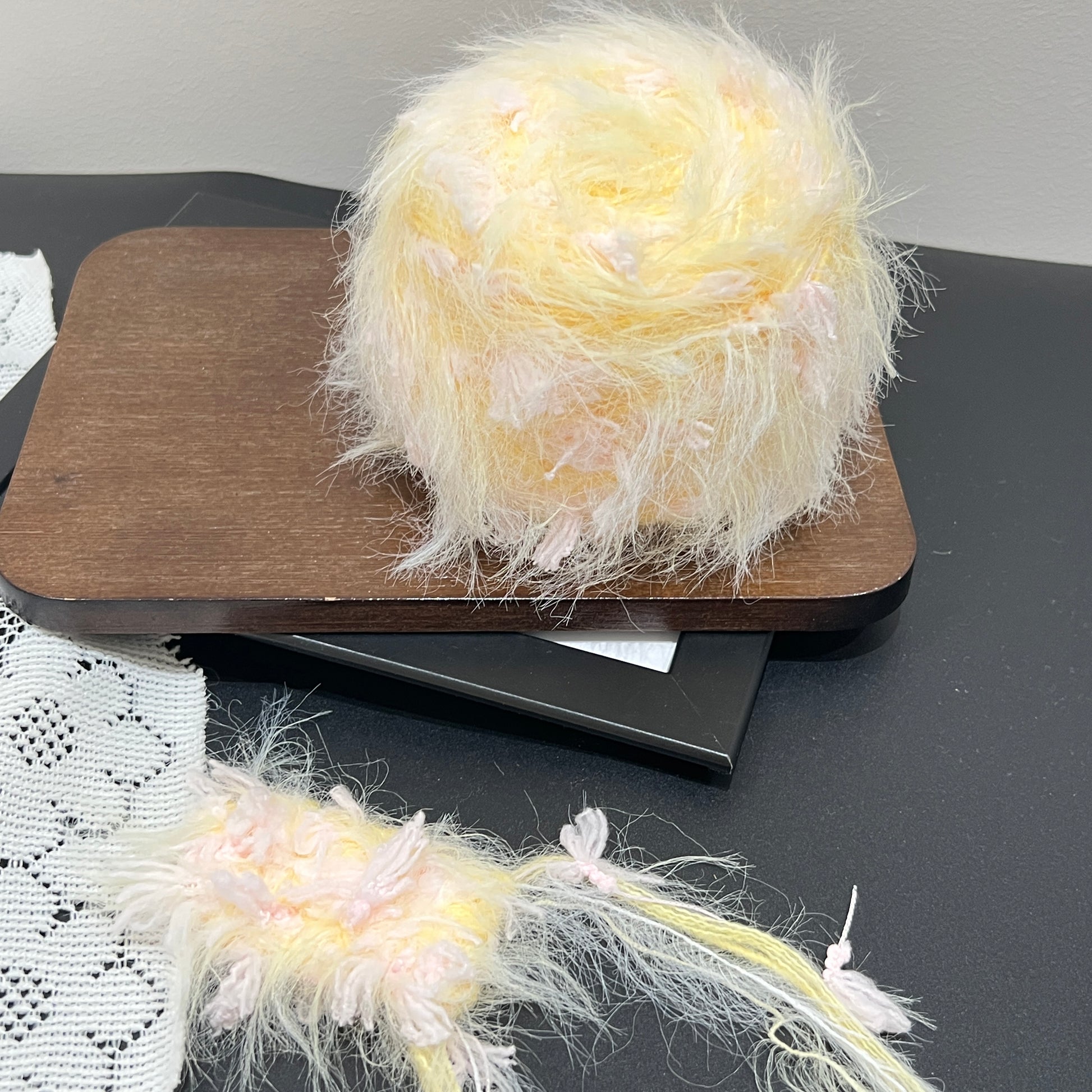 Pastel yellow pink floral multi-strand hand-blended cake yarn placed on wooden board