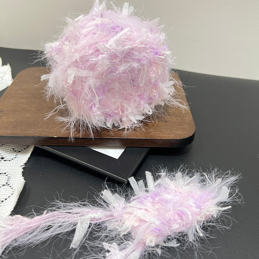 Pastel lavender iridescent floral multi-strand hand-blended cake yarn placed on wooden board with dark counter backdrop