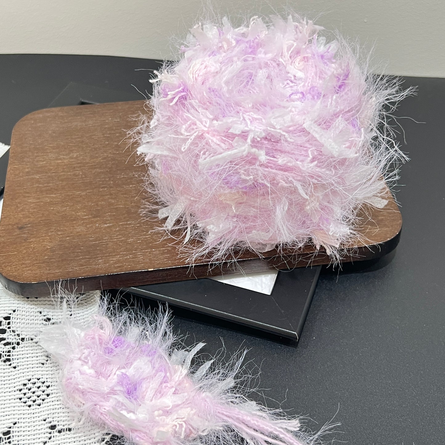 Layout shot of lavender iridescent yarn cake and matching fiber swatch beside hollow white lace fabric