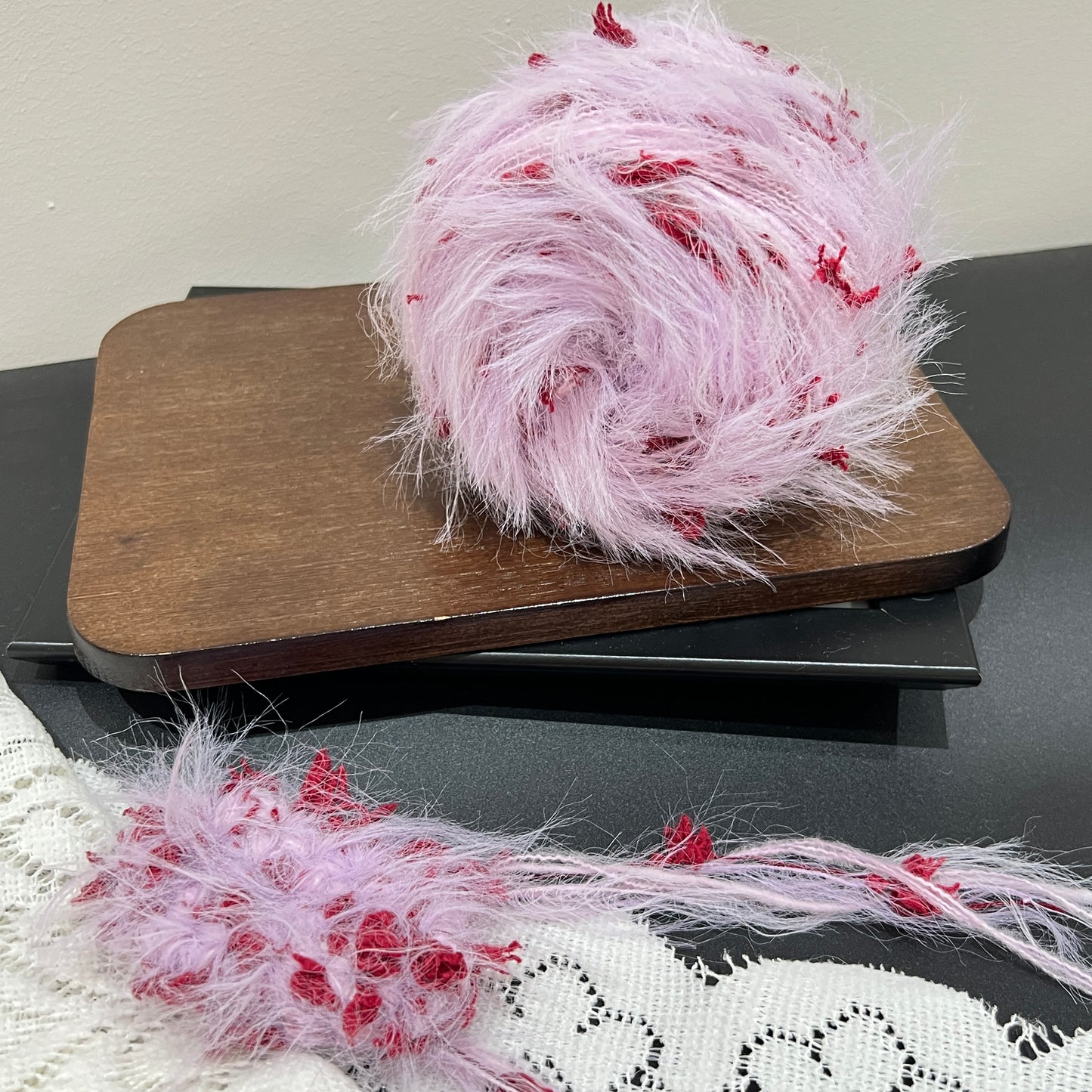 Pastel lilac crimson floral multi-strand hand-blended cake yarn placed on wooden board with dark counter backdrop