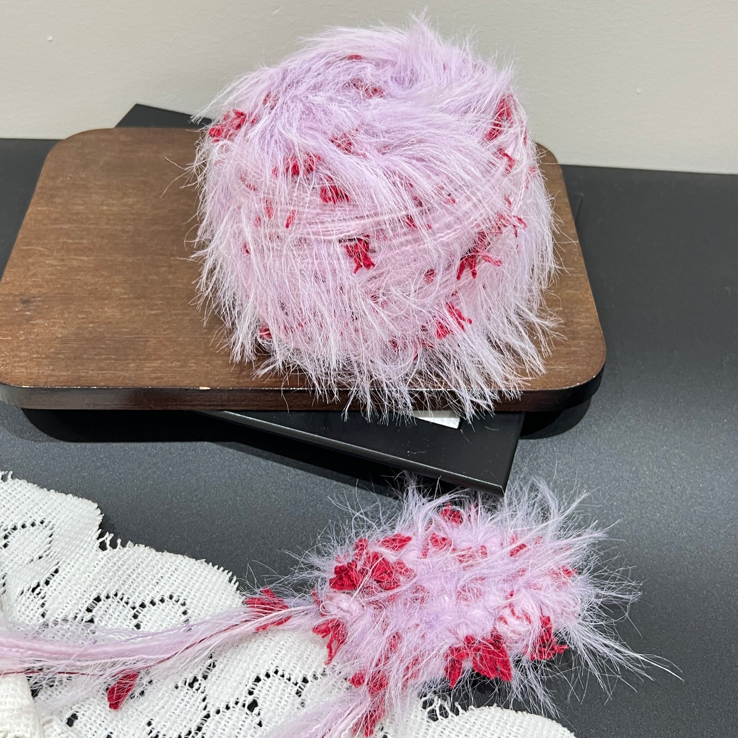 Layout shot of lilac crimson yarn cake and matching fiber swatch beside hollow white lace fabric