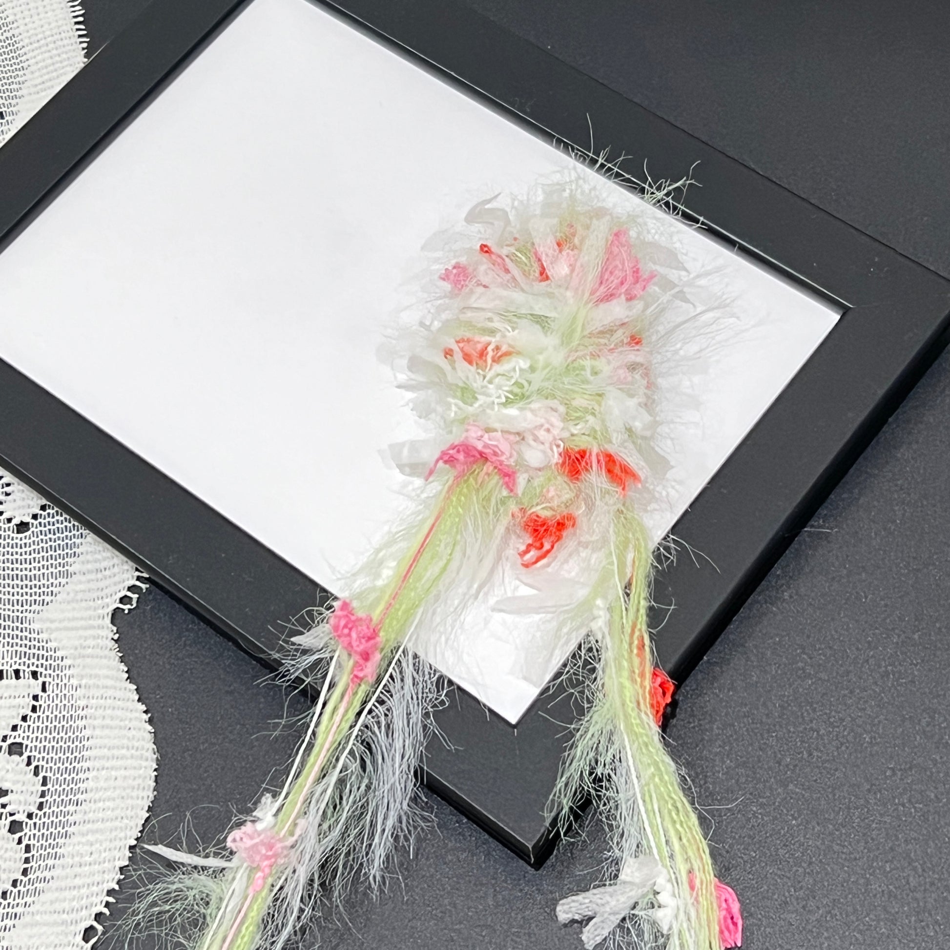 Close-up macro shot of lime pink coral fiber swatch mounted inside black thin photo frame, long feathery fuzzy strands and multi-tone petal details