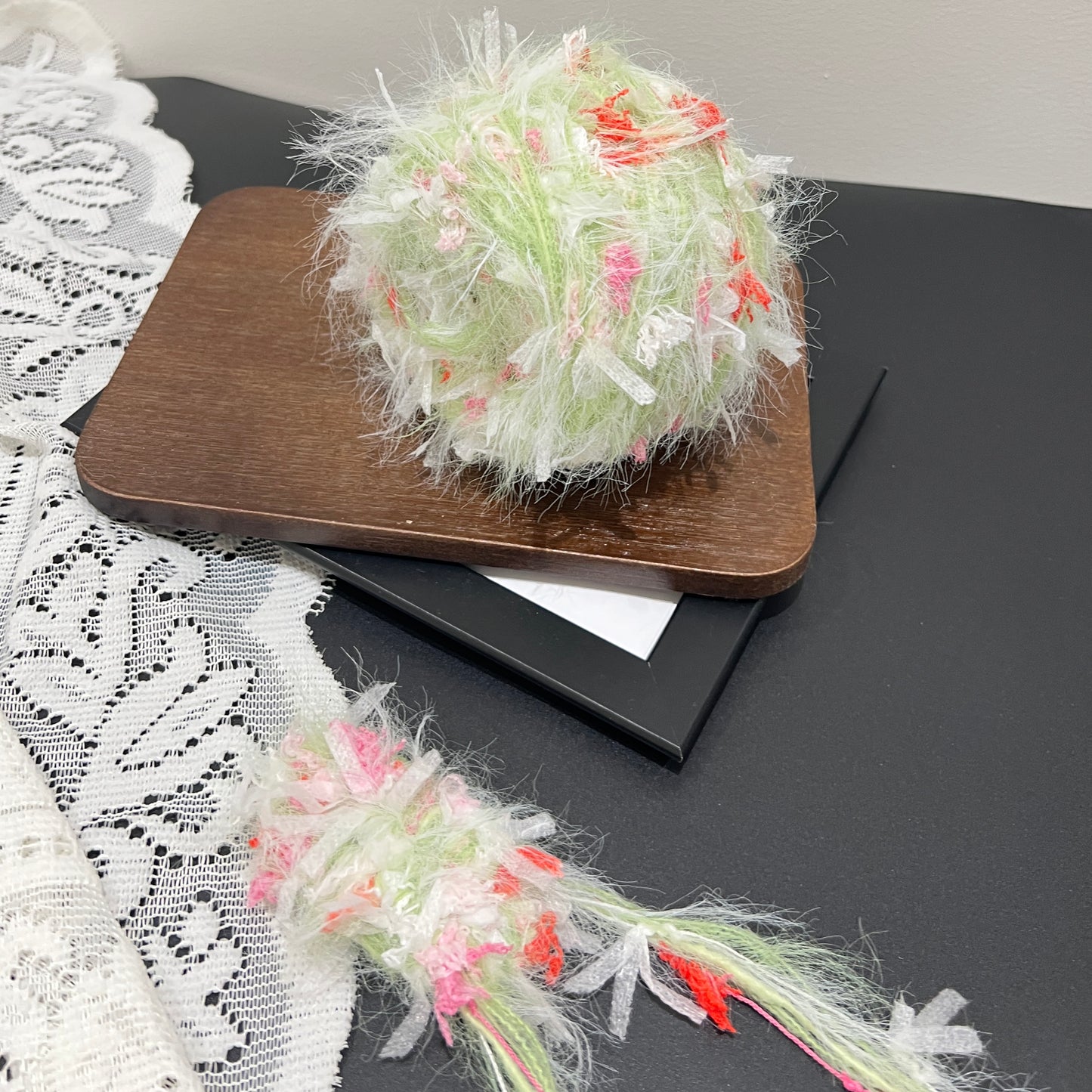 Front overhead spherical shot soft pastel lime base hand-blended yarn ball mixed with blush pink & coral red petal ribbon fiber accents, airy layered fuzzy texture